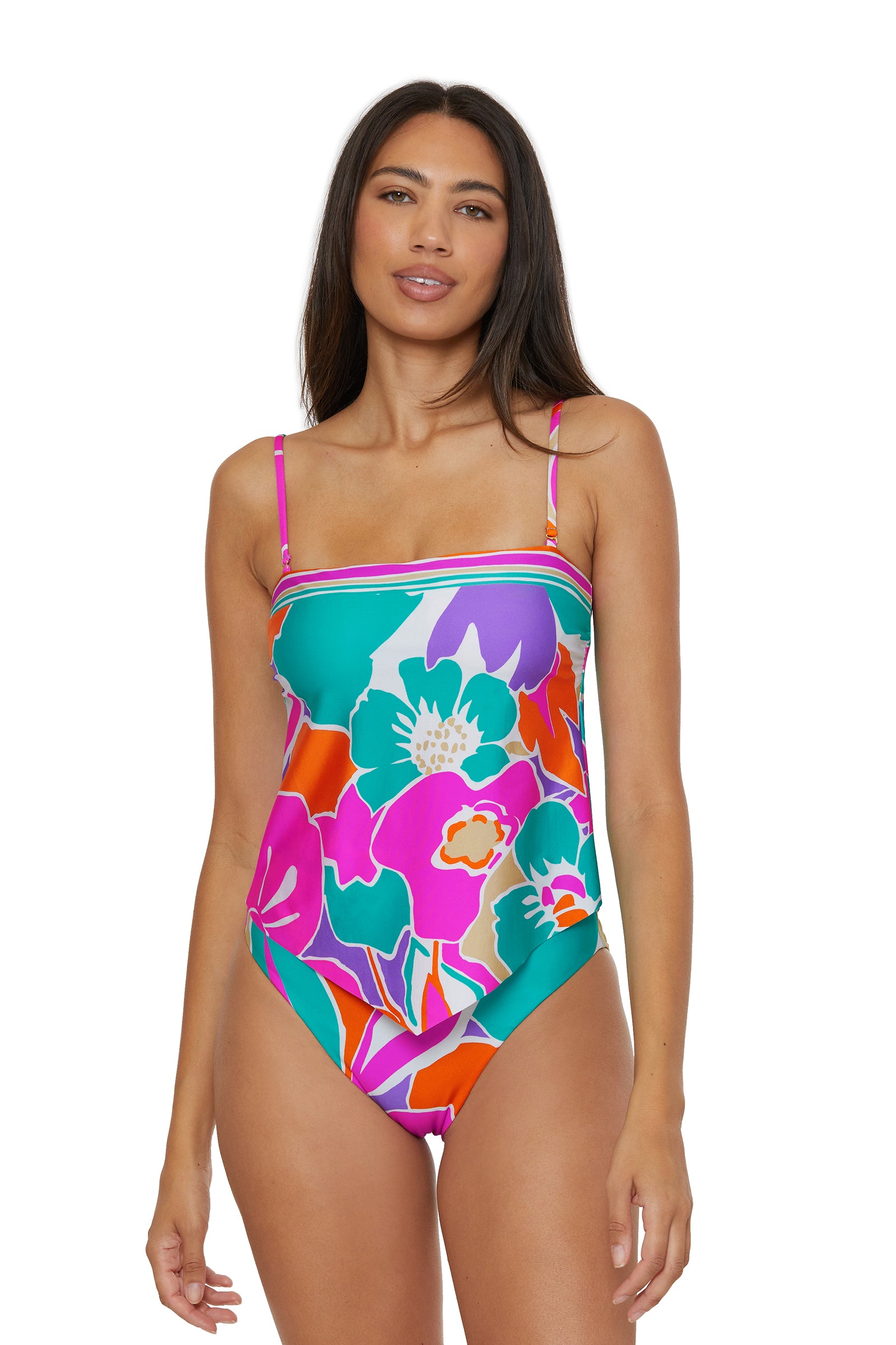 A woman wearing the TRINA TURK SWIM Handkerchief Tankini Swim Top - Amalfi, which features vibrant pink, green, orange, purple, and white patterns with thin straps, stands facing forward and smiles slightly.