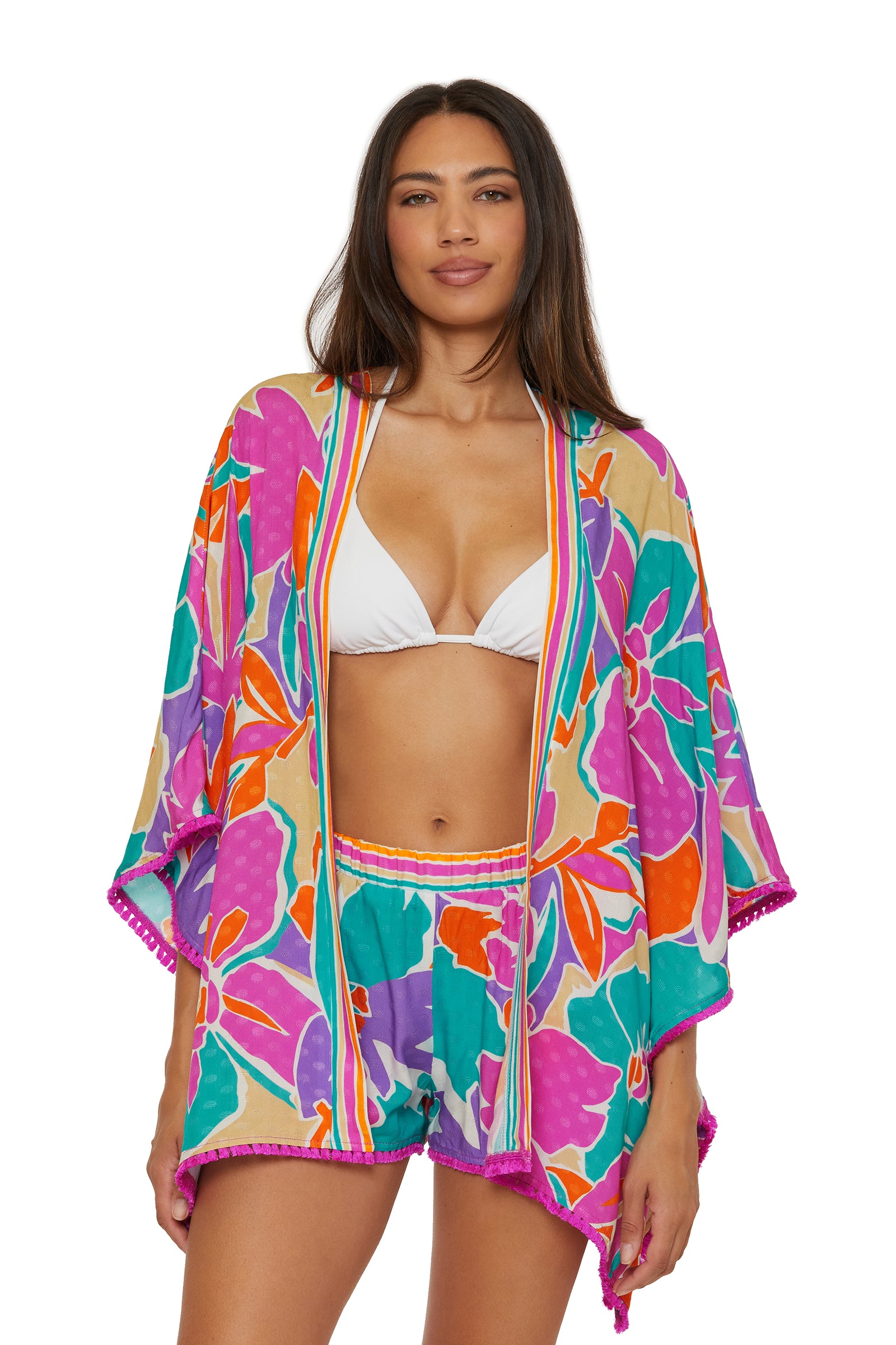 A woman wearing a white bikini top and the Amalfi Swim Cover-Up Short, featuring a matching colorful floral kimono and shorts set with purple, orange, and green patterns, standing and smiling at the camera.
