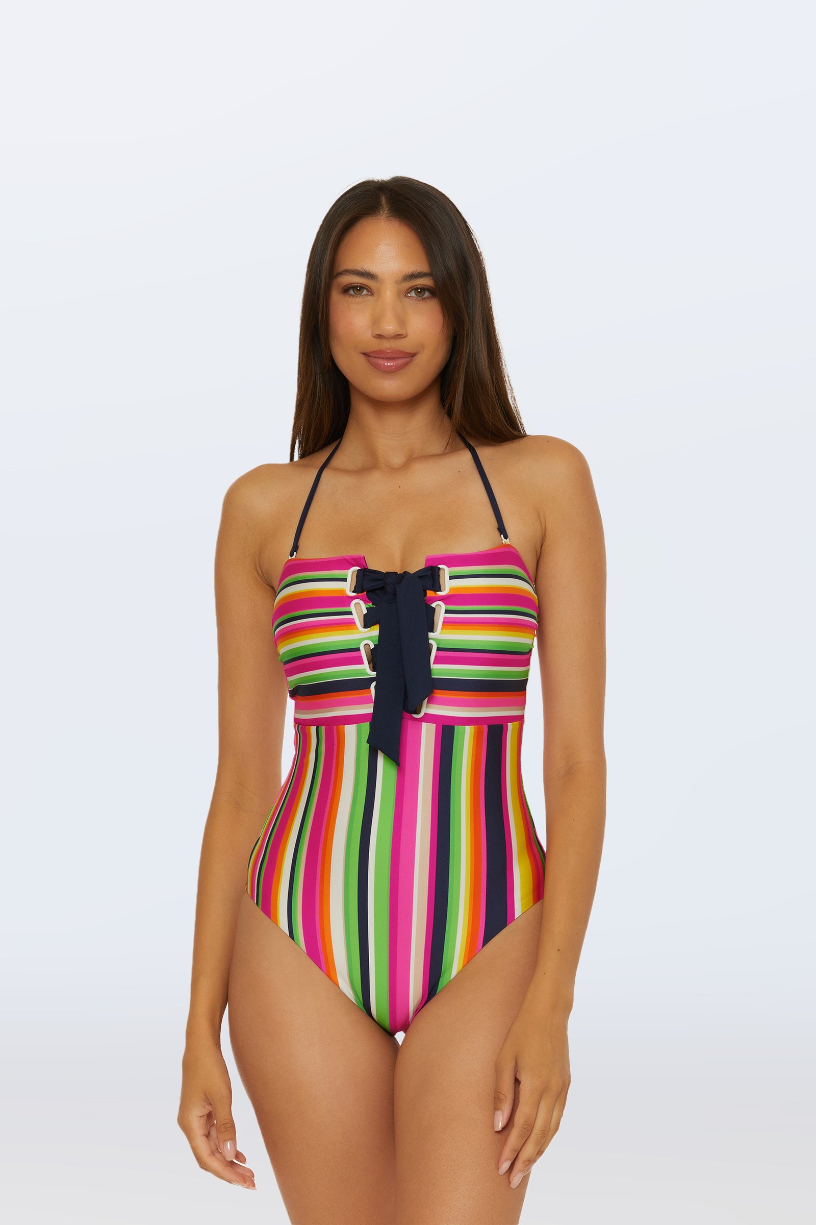 A woman models the Bandeau One-Piece Swimsuit - Splash Stripe in multi, featuring colorful stripes and a front lace-up detail, set against a light background.