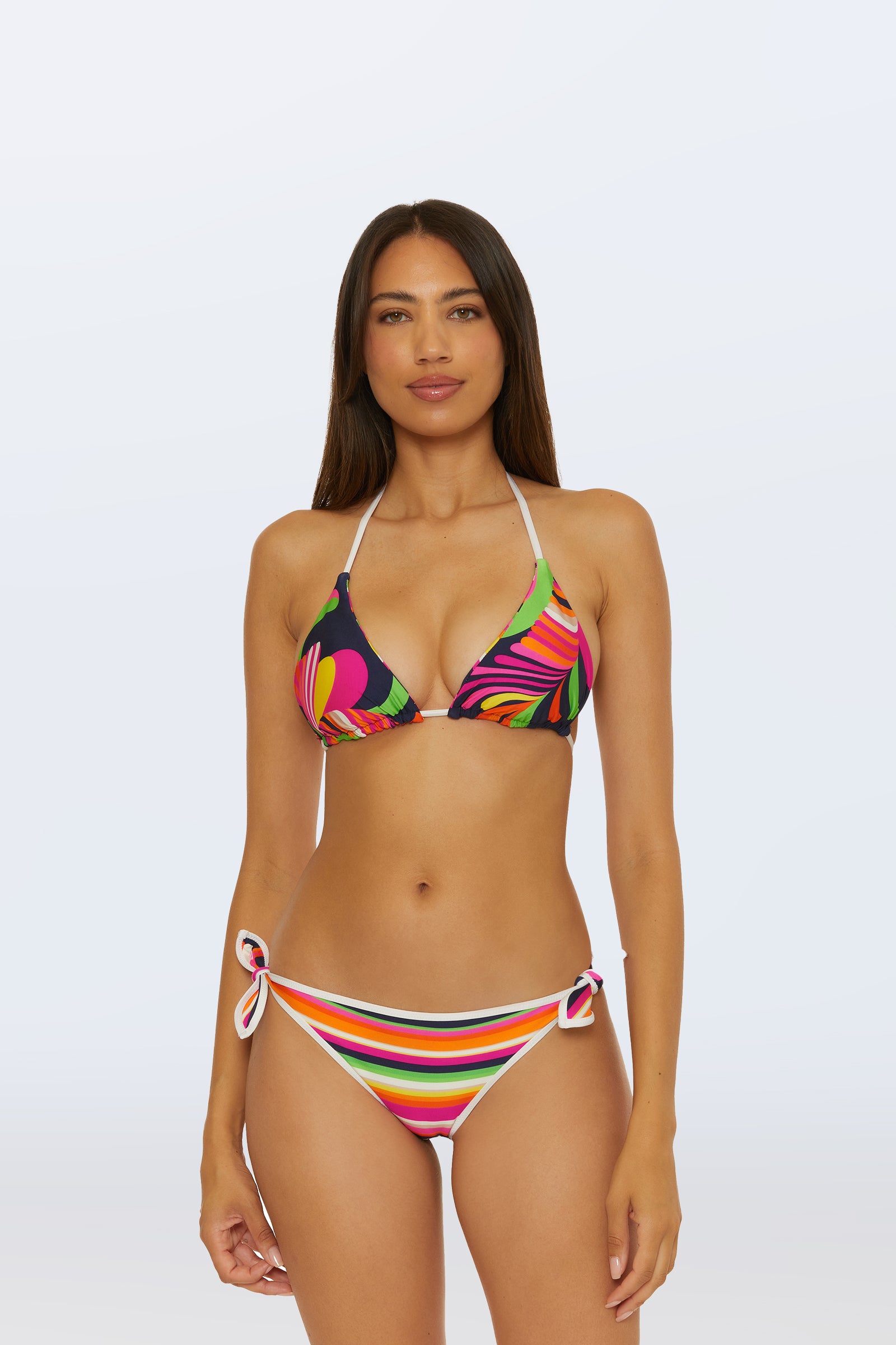 A woman with long brown hair models the Reversible Triangle Swim Top - Splash Stripe, featuring a retro swirl print, paired with multicolored striped bottoms against a plain light background.