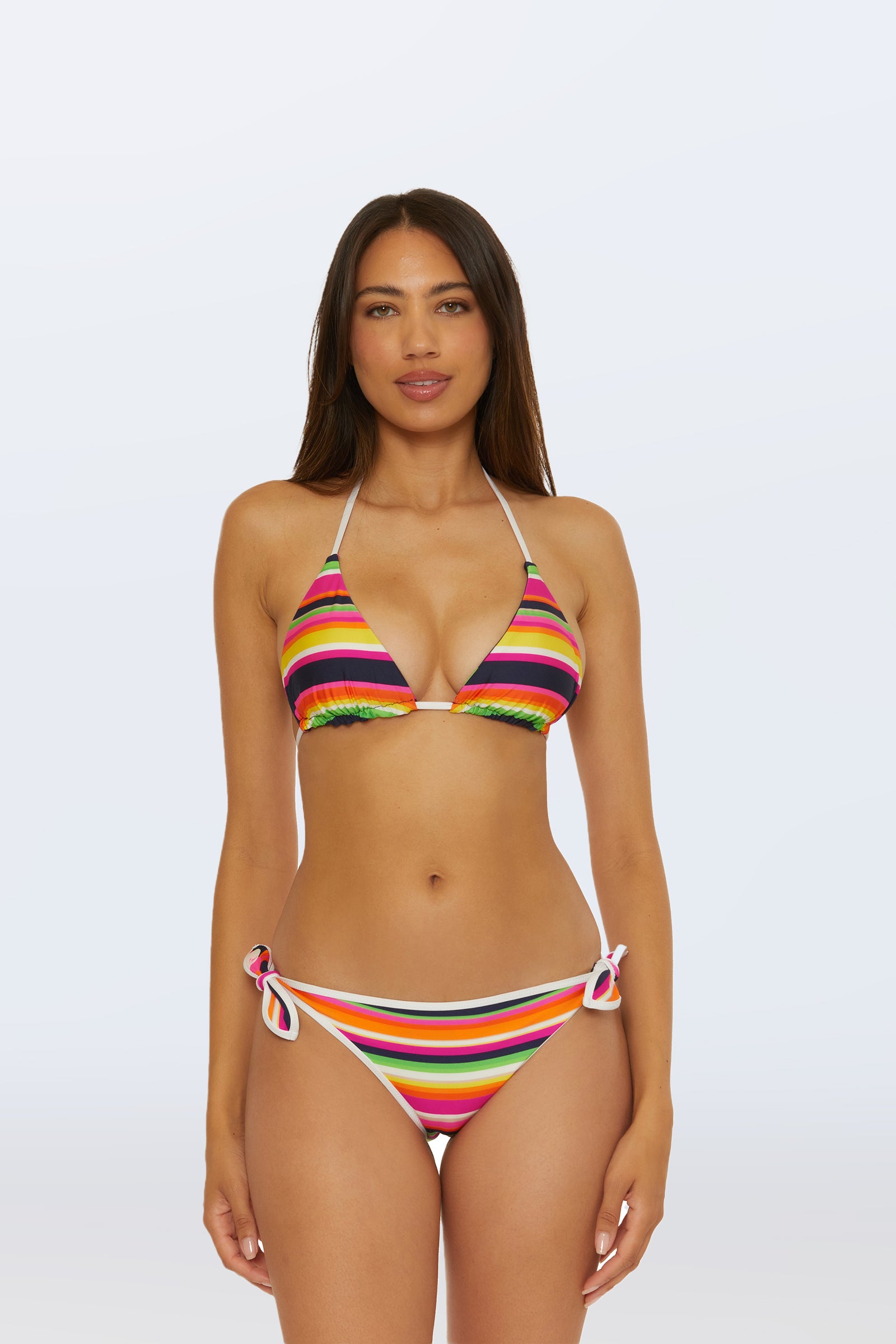 A woman faces forward against a plain light background, wearing the Reversible Tie Side Swim Bottom in Splash Stripe, featuring colorful stripes and side-tie details. She has long, straight hair and a neutral expression.