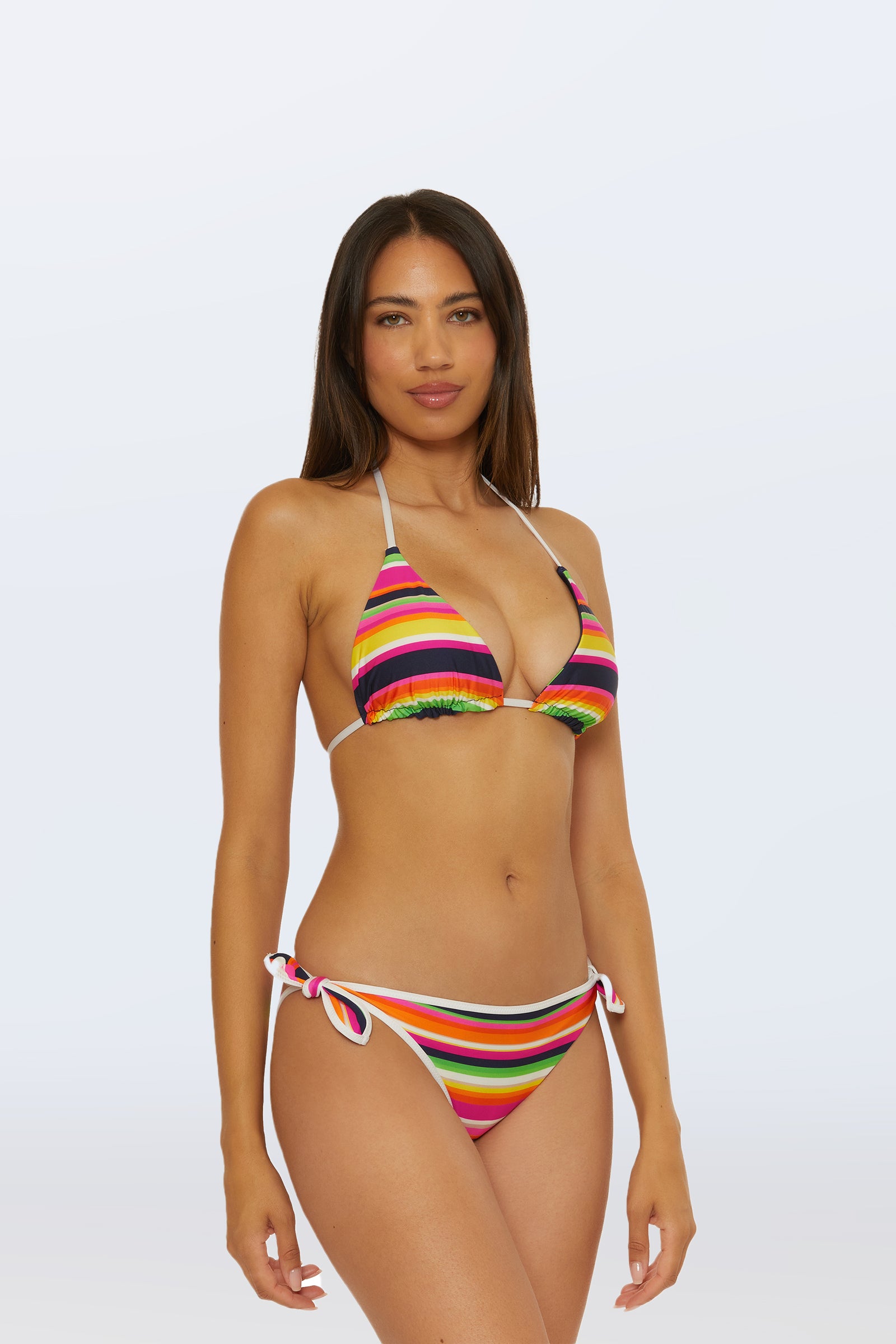 A woman with long brown hair models the Reversible Triangle Swim Top in Splash Stripe, featuring a halter neck and paired with side-tie bottoms. She stands against a plain light background, looking at the camera with a neutral expression.