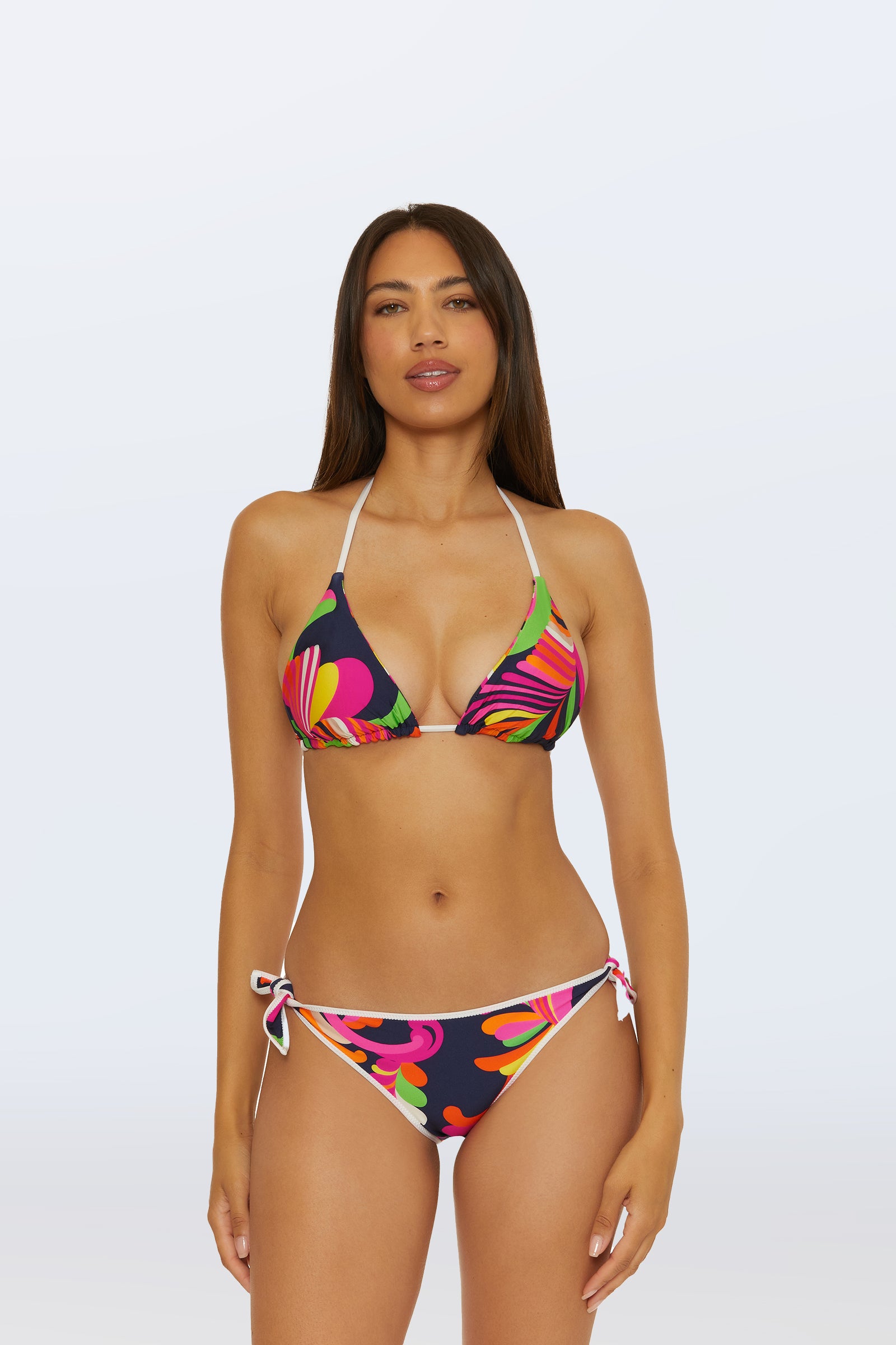Woman stands facing forward in the Reversible Tie Side Swim Bottom - Splash Stripe, featuring colorful stripes and adjustable tie sides, against a plain light background. She has long straight hair and a neutral expression.