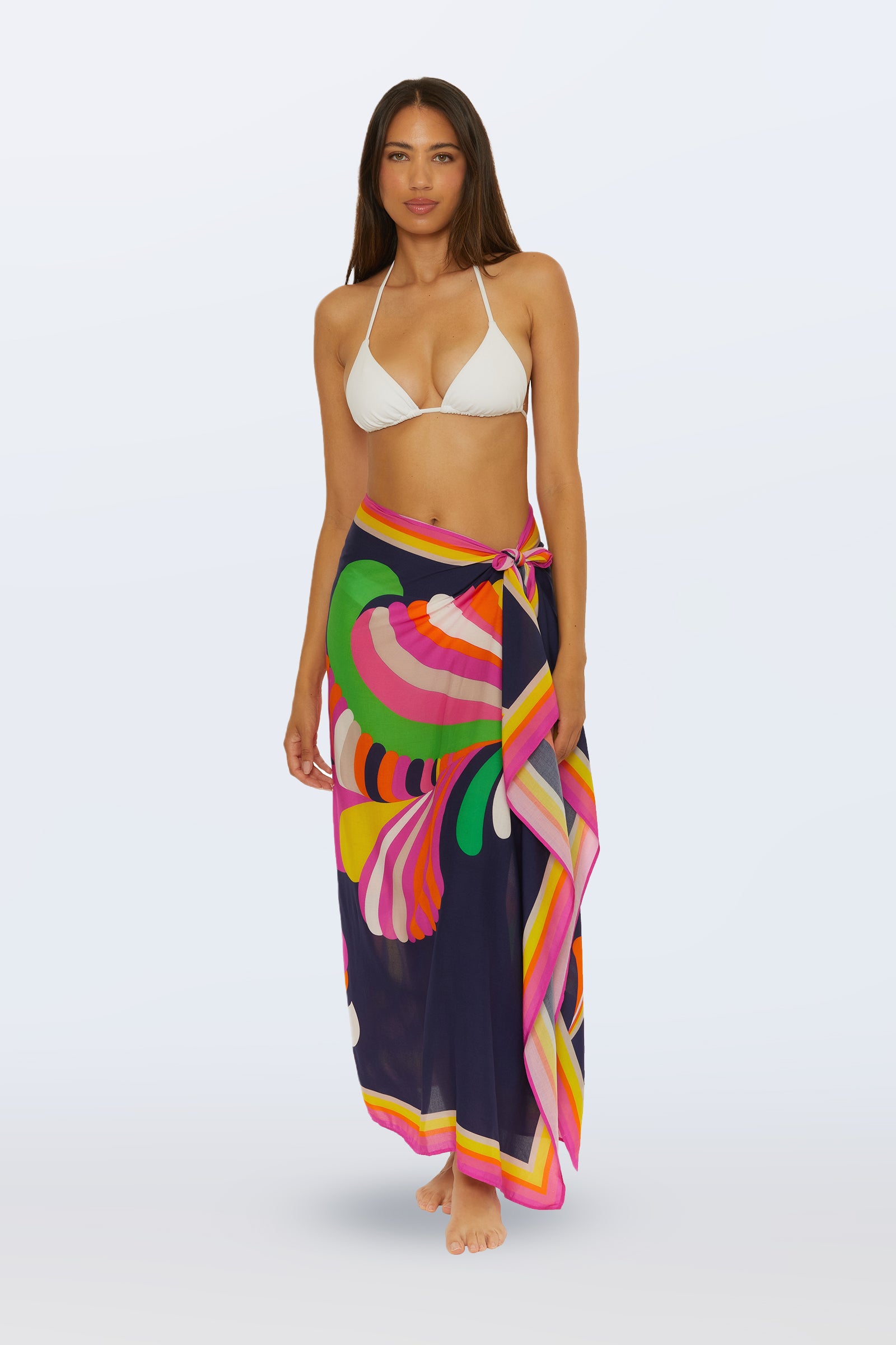 A woman in a white bikini top and the Pareo Swim Cover-Up - Palms Paradise (Multi) stands barefoot against a light background.