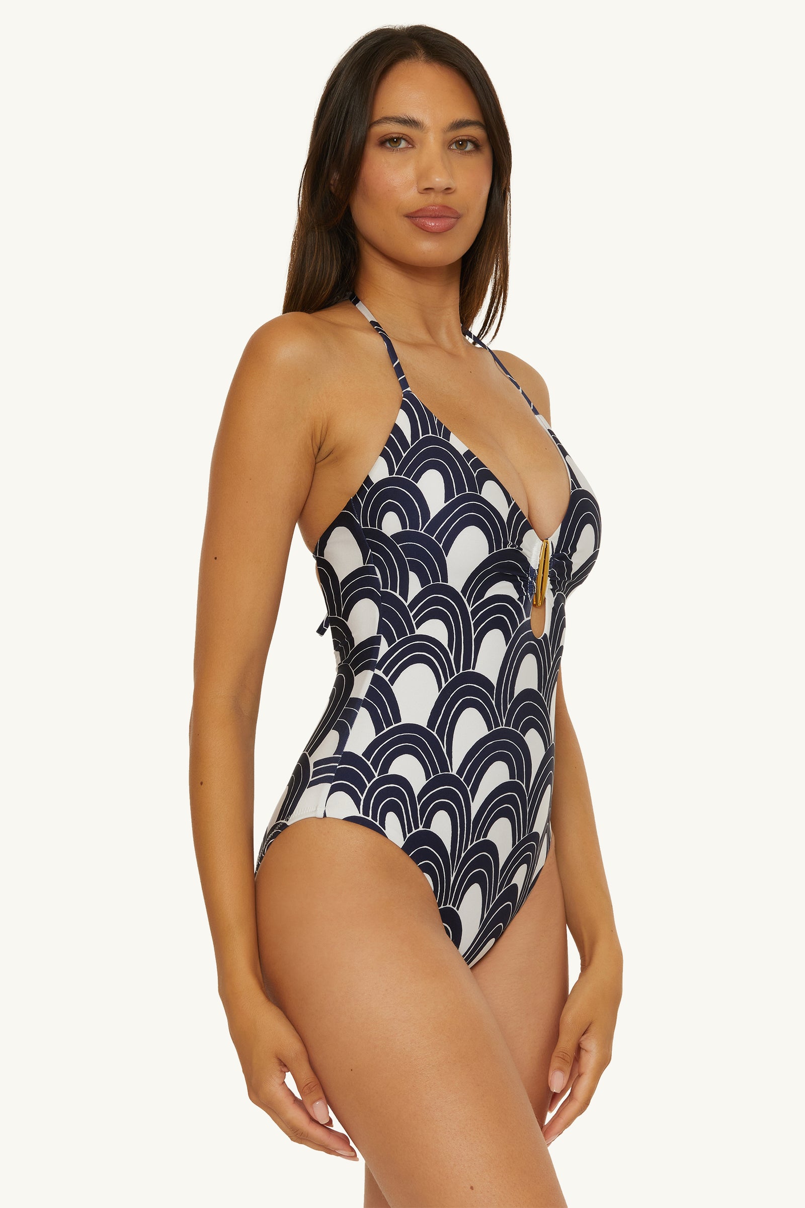 A woman models the Buckle One-Piece Swimsuit - Arches, featuring a navy and white wave pattern and a deep V-neckline, against a plain light background.