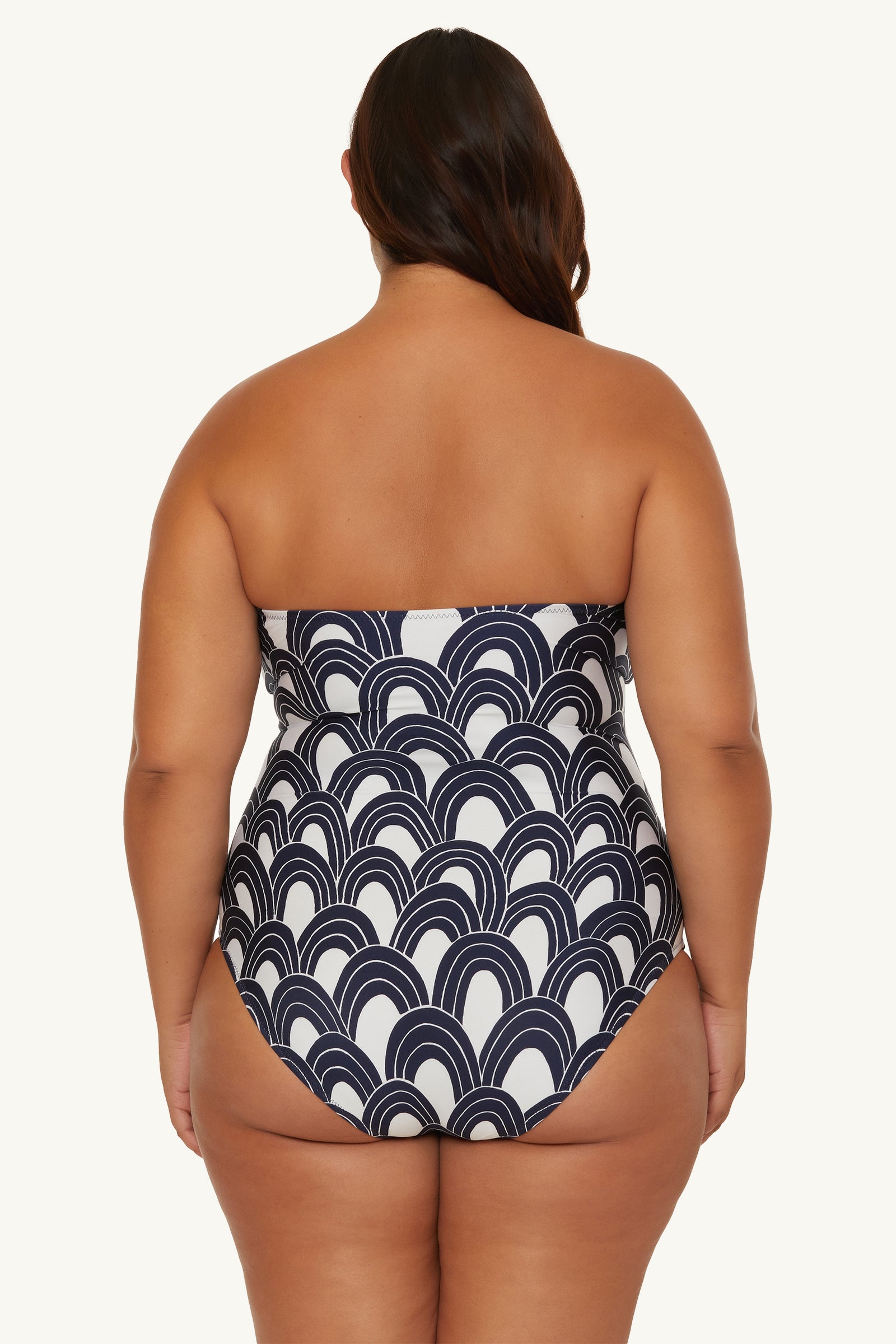A woman with long, dark hair models the Lace-Up Bandeau One-Piece Swimsuit - Arches, featuring a navy and white geometric wave pattern, shown from the back against a plain light background.