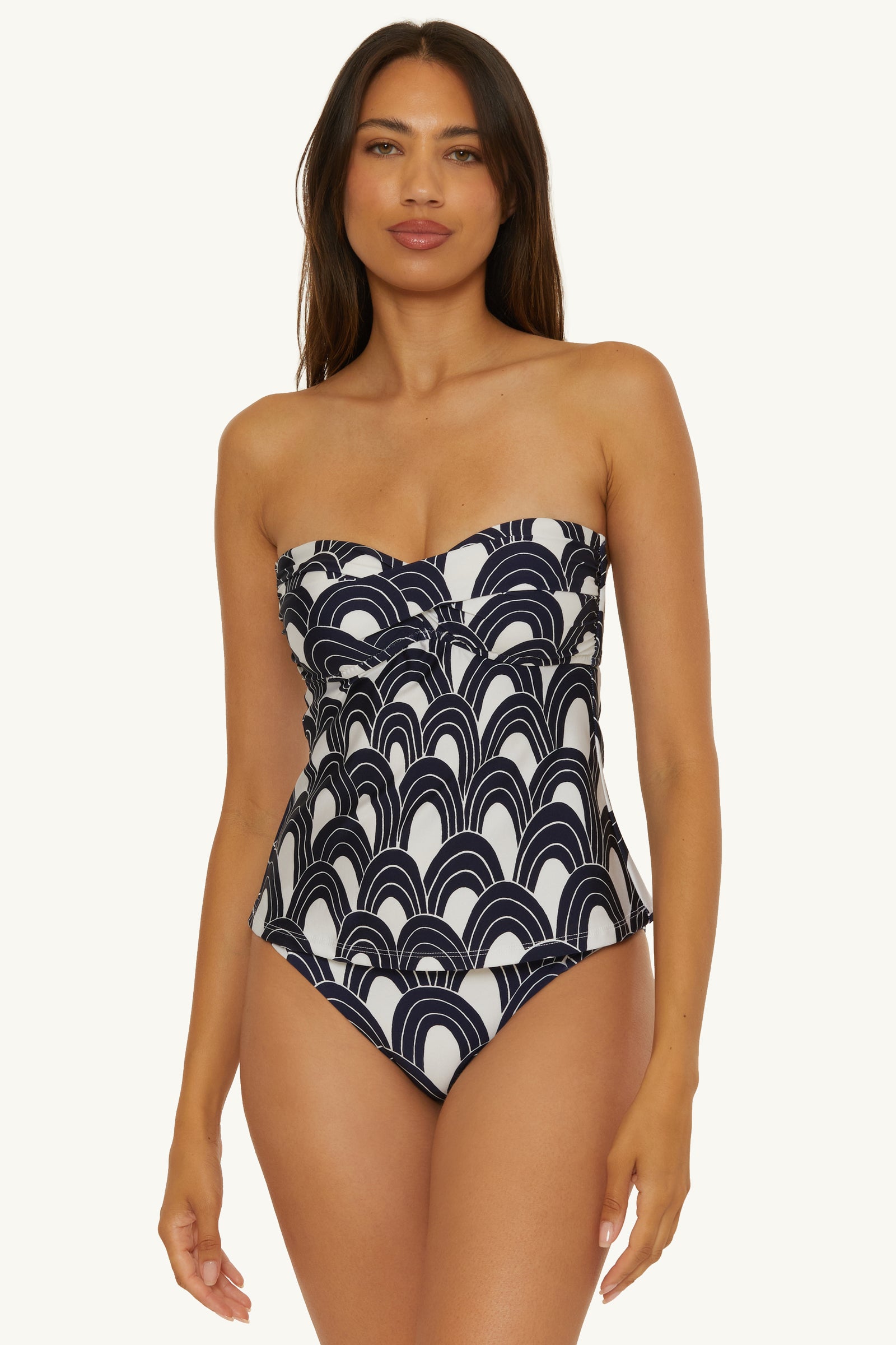 A woman wears the Twist Bandeau Tankini Swim Top in Arches Swim, featuring a black and white geometric wave pattern, standing against a plain, light background.