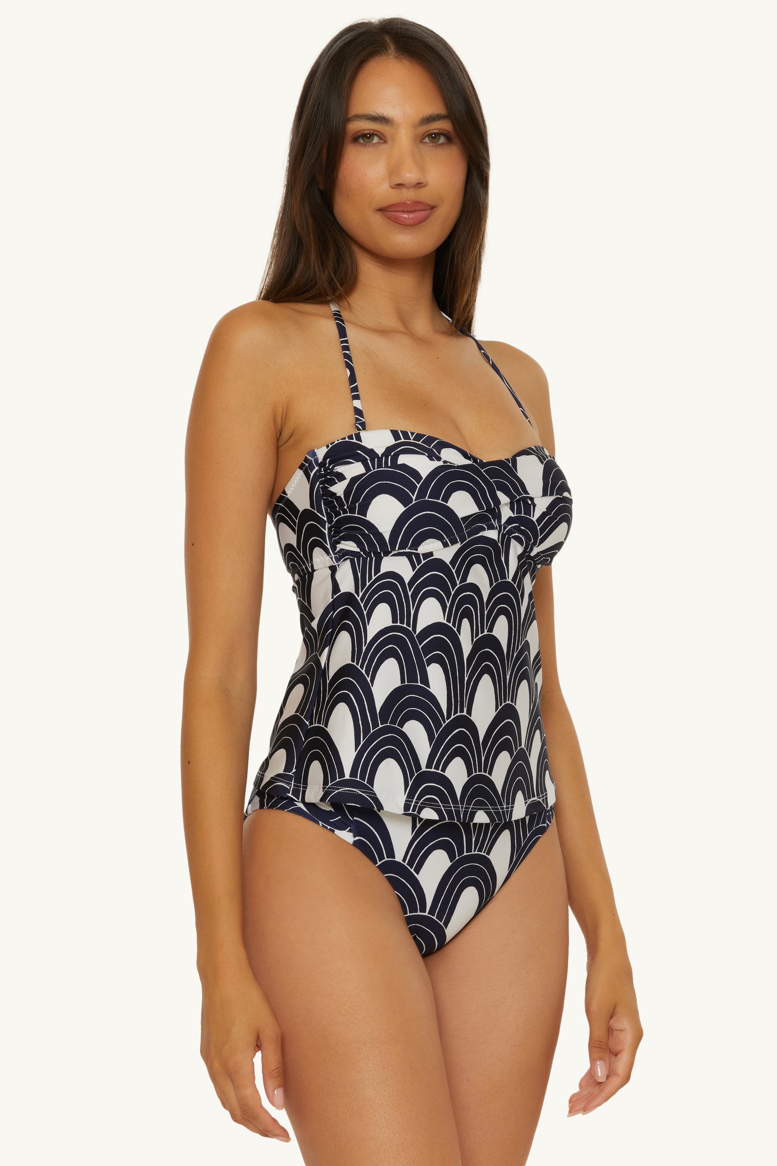 A woman wears the Twist Bandeau Tankini Swim Top - Arches, featuring a navy and white abstract wave pattern with spaghetti straps and a fitted design, standing against a plain white background.