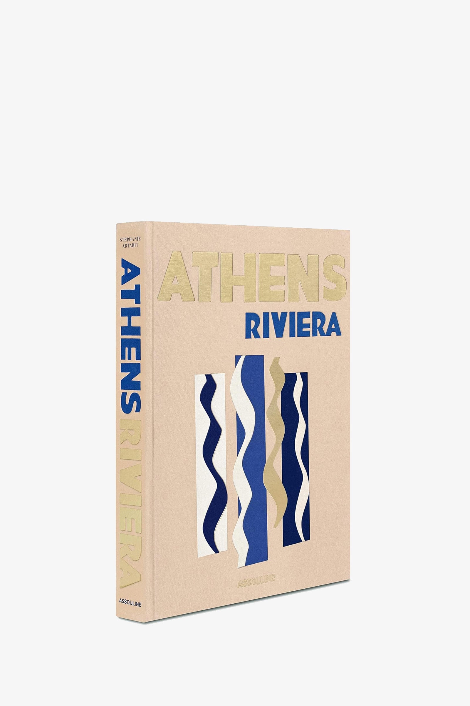 An Assouline Athens Riviera Book, in beige with gold and blue lettering, stands upright against a white background. Its cover features abstract wavy shapes in blue, white, and beige.