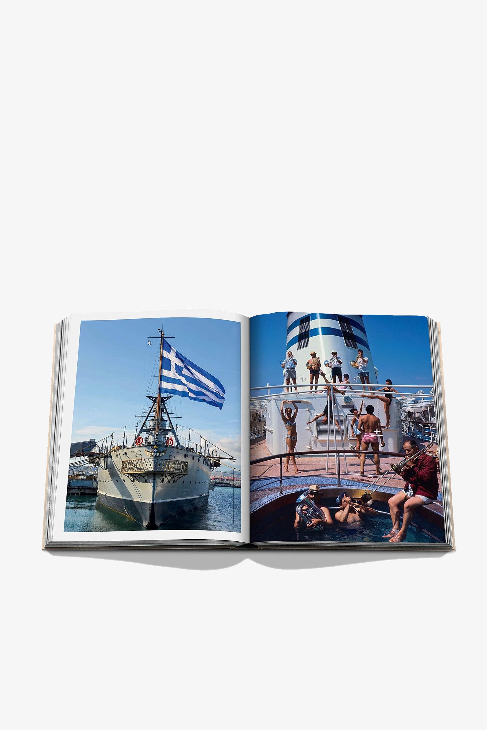 An open copy of the Assouline Athens Riviera Book displays an image of a ship with a Greek flag on the left page and a lively scene of people enjoying themselves on a cruise ship deck on the right page.