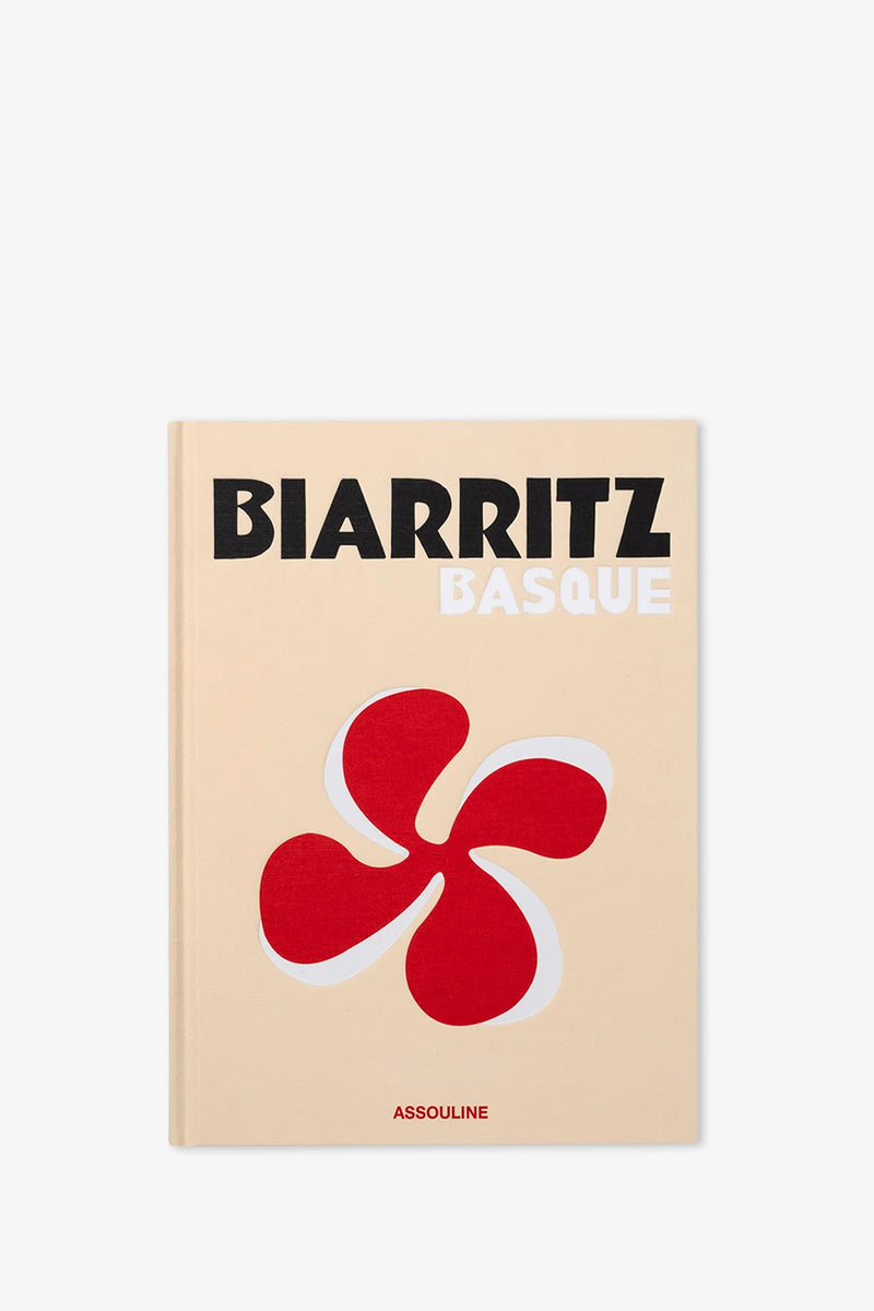 The Assouline Biarritz Basque Book features a beige cover with "BIARRITZ BASQUE" in bold black and white text, a striking red abstract symbol, and "ASSOULINE" displayed at the bottom.
