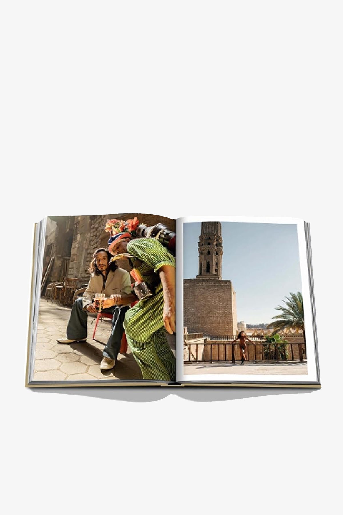 An open Assouline Cairo Eternal book displays two people in colorful clothing on a stone street on the left page and a historic minaret against a clear blue sky with palm trees on the right.