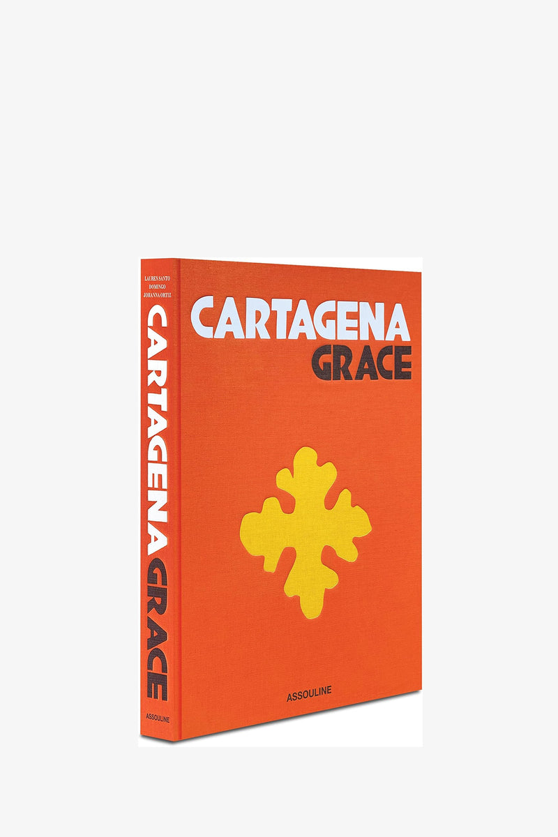 The Assouline Cartagena Grace Book features a bright orange hardcover with bold white and black text and a large yellow abstract shape on the front cover; the publisher ASSOULINE is displayed at the bottom.