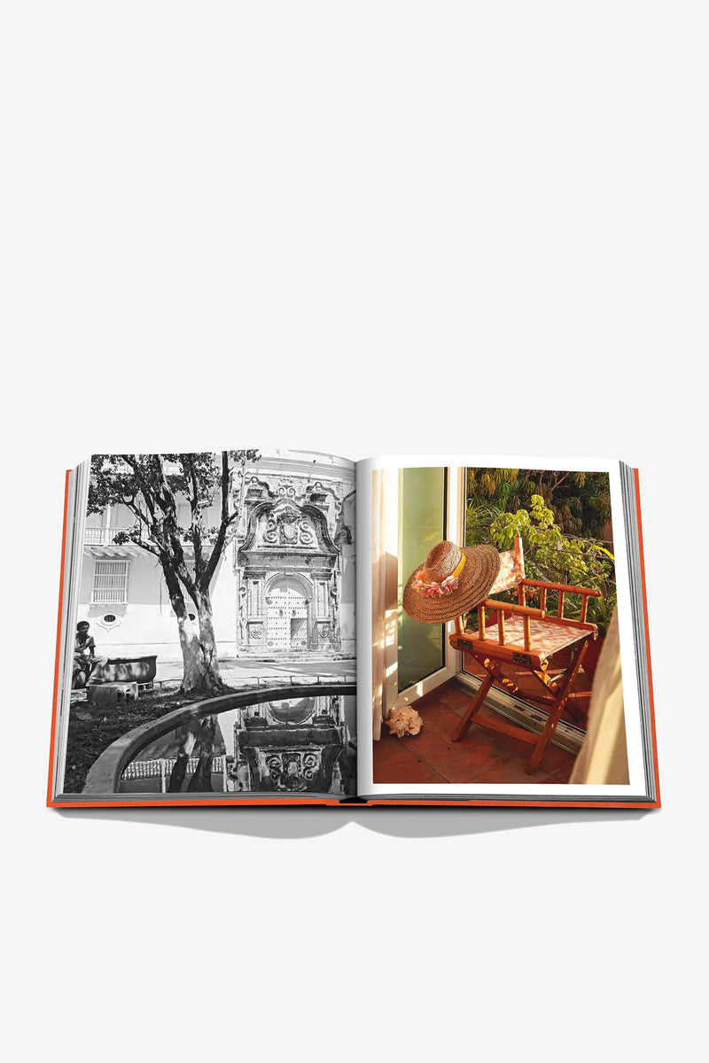 An open Assouline Cartagena Grace Book displaying a black-and-white photo of a building with a pond on the left page and a color photo of a wooden rocking chair adorned with a hat and red scarf on a porch on the right page.