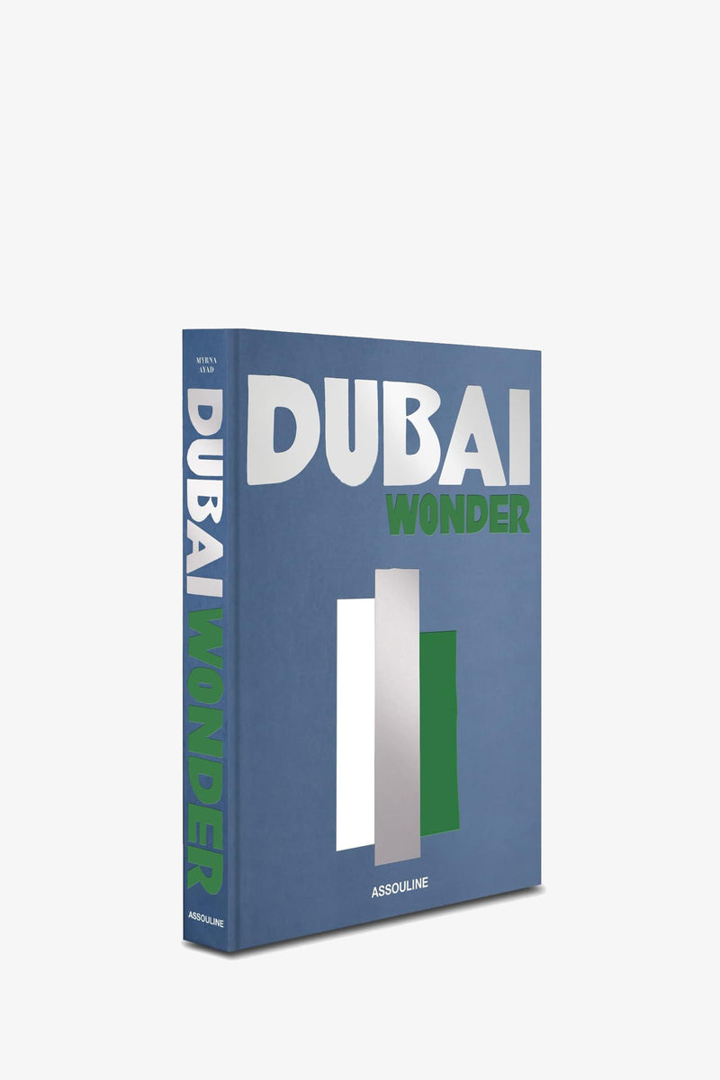 An Assouline Dubai Wonder book, featuring a blue cover with bold silver and green text and graphic shapes, stands upright against a plain white background.