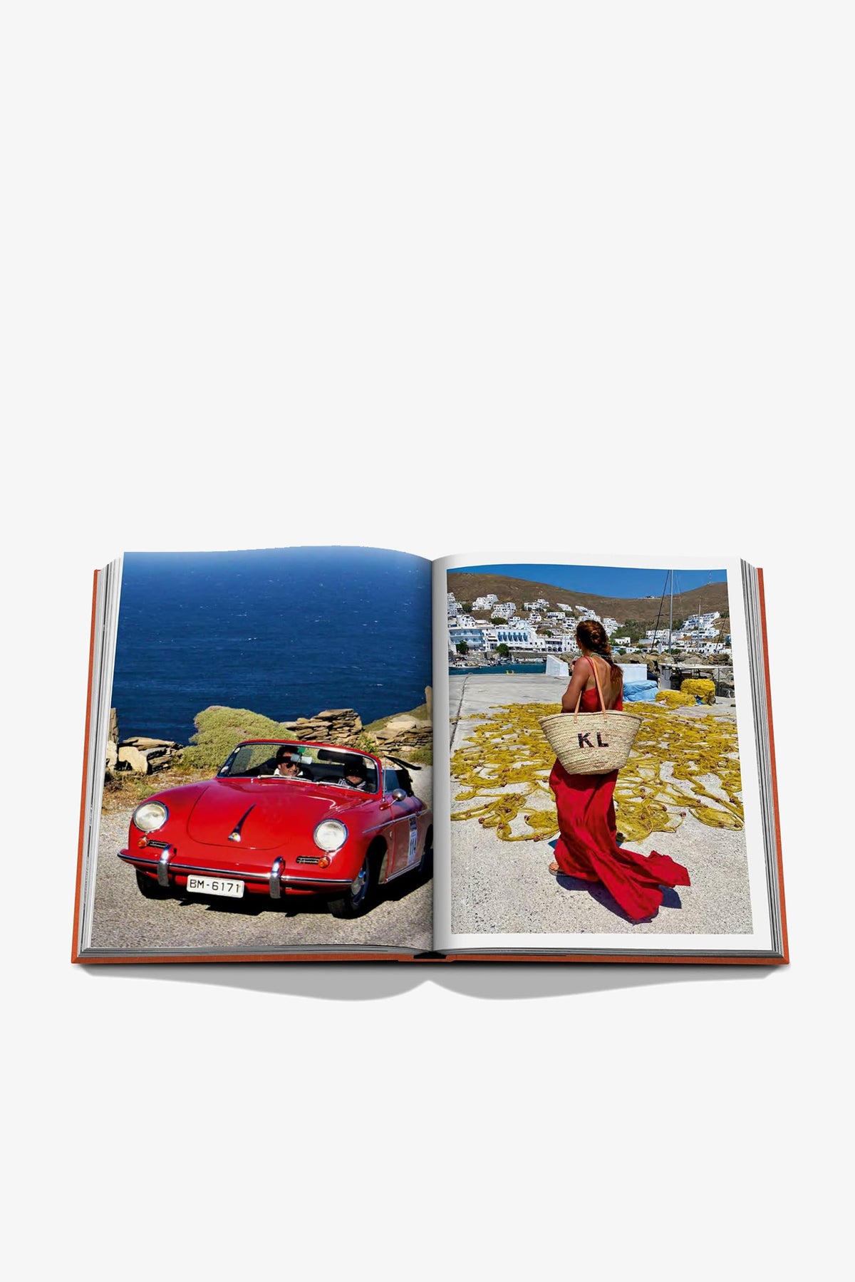 An open copy of ASSOULINE GREEK ISLANDS displays a red vintage convertible parked by the sea on the left page, while the right page features a woman in a red dress holding a large tote bag as she strolls along the shoreline.