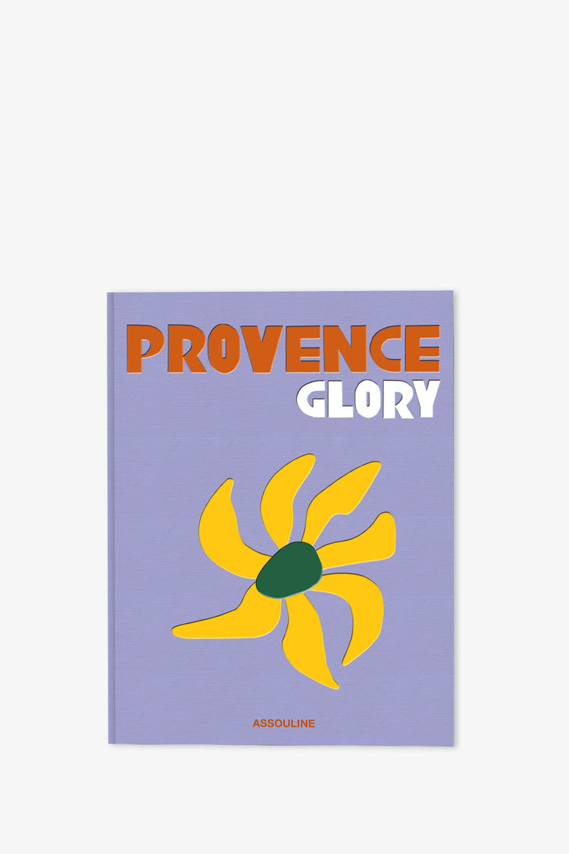 The Assouline Provence Glory Book features bold orange and white text on a lavender cover, accented with a yellow abstract sun-like design with a green center, and ASSOULINE written at the bottom.