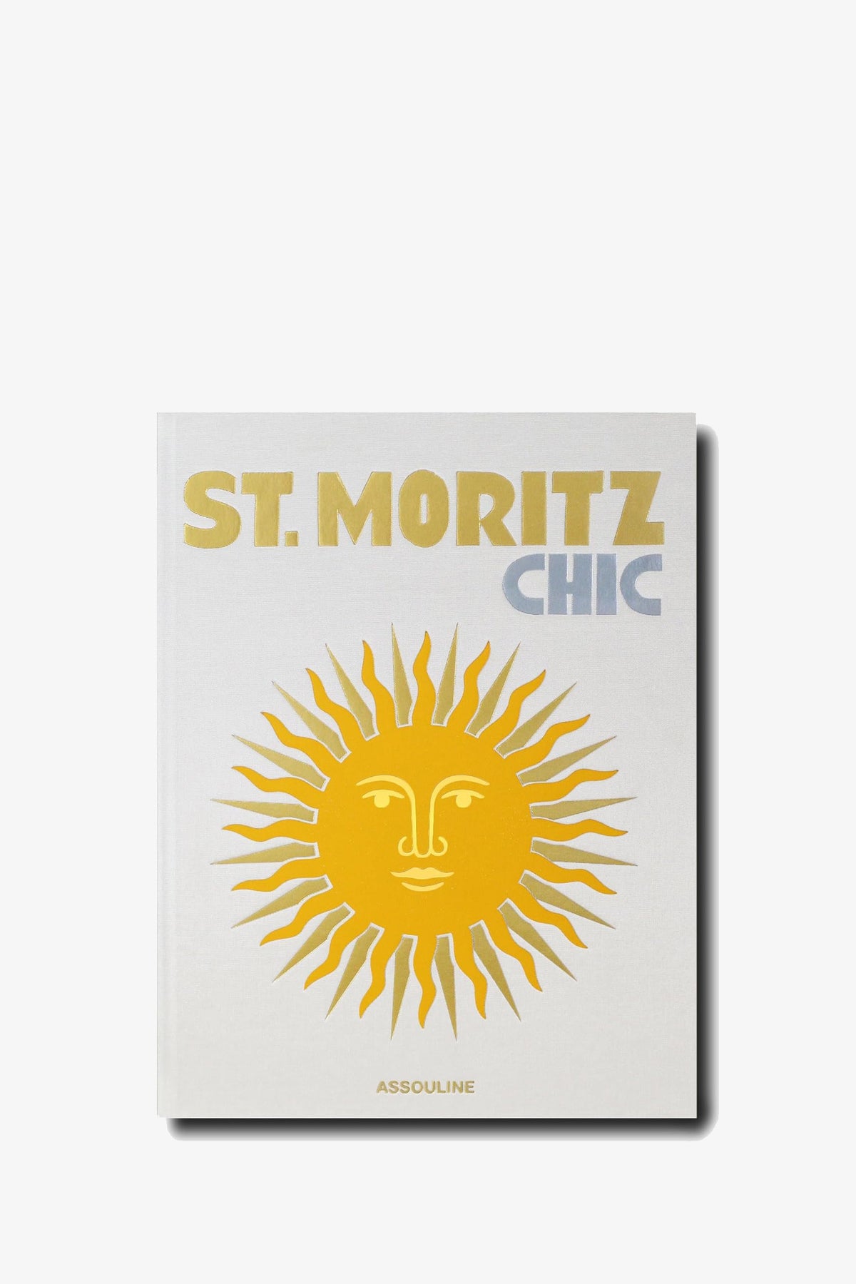 The Assouline St Moritz Chic book features a white cover with the title “ST. MORITZ” in gold and “CHIC” in pale blue above a large golden sun with a face, with the publisher ASSOULINE at the bottom.