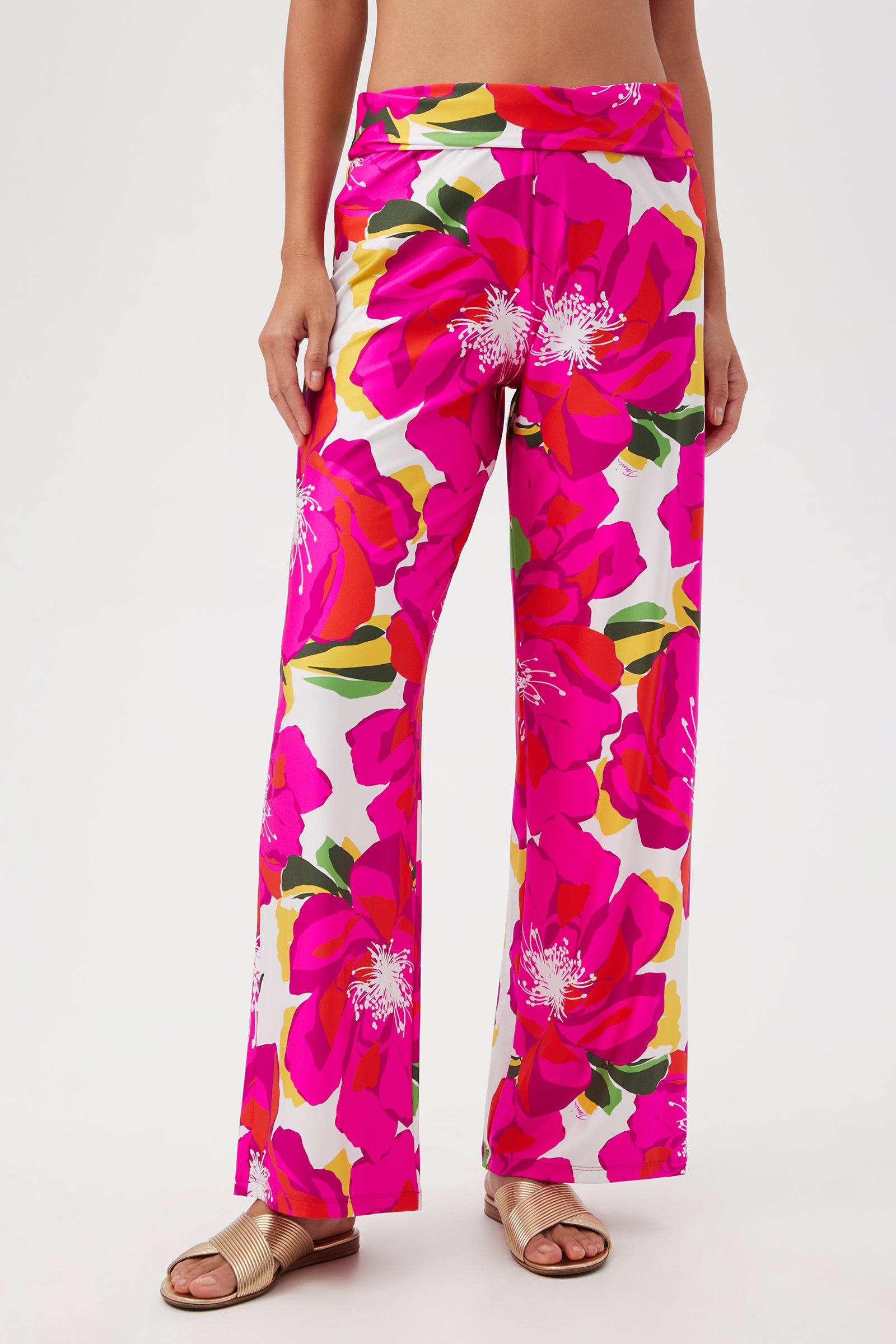 A person wears the Bloom Swim Pant in Multi, featuring a bold floral print and wide-leg fit, paired with beige slide sandals. The image is cropped from the chest down—perfect as a chic swim cover-up for poolside lounging.