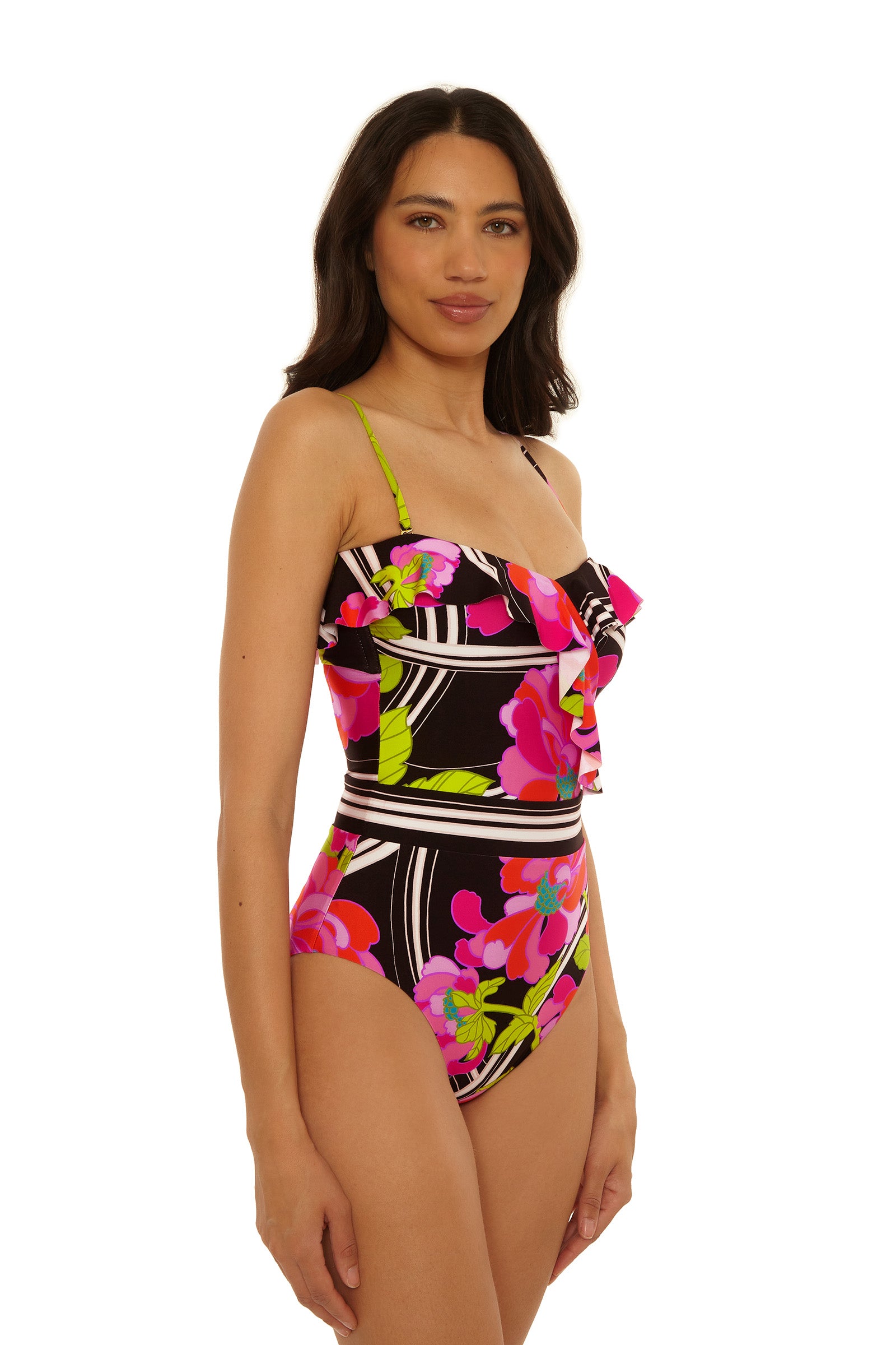 A woman models the Bandeau One-Piece Swimsuit - Bougainvillea, featuring a black base with bold pink, red, and green floral patterns and ruffle bust details, against a plain white background.