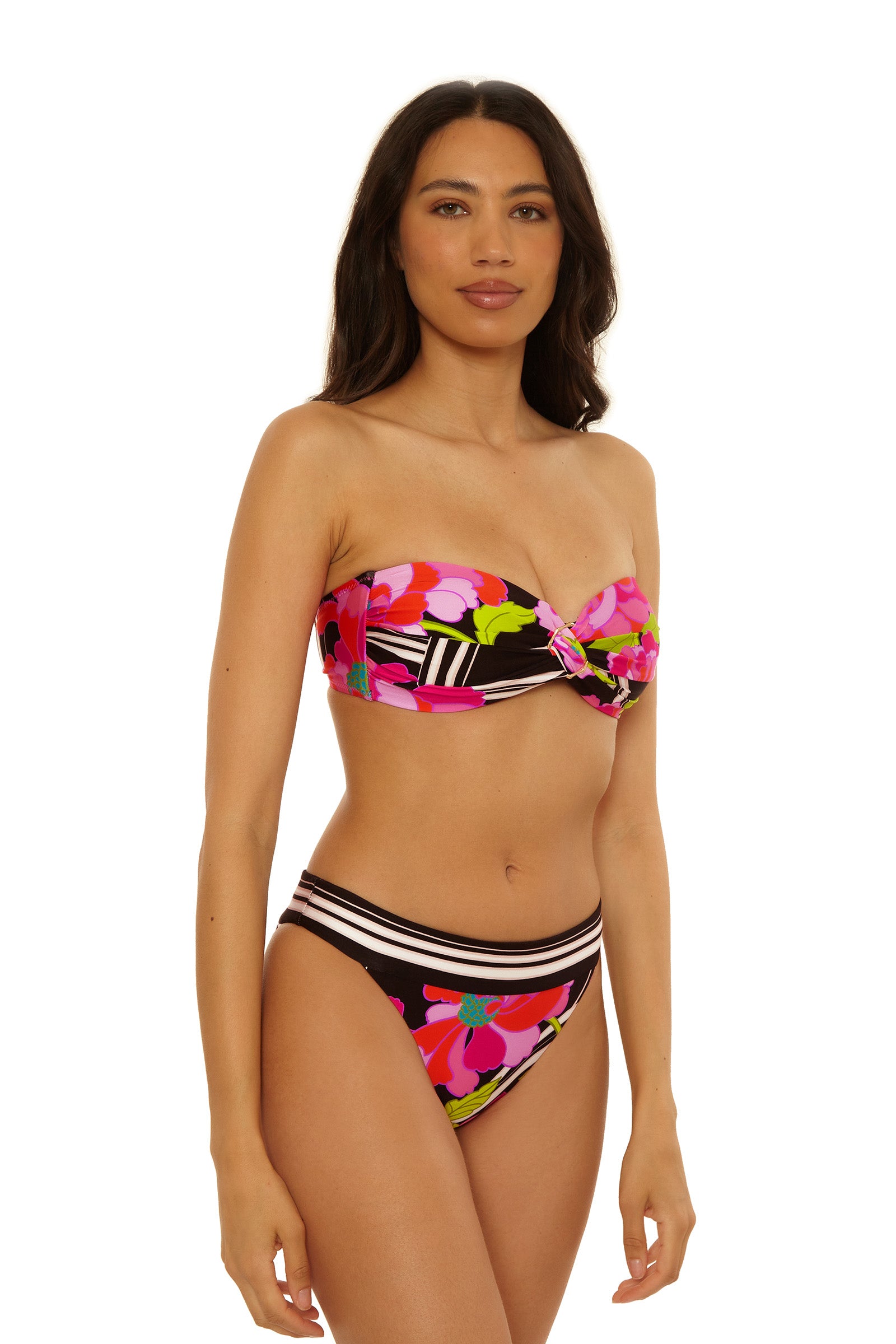 A woman models the Reversible Hipster Swim Bottom - Bougainvillea, featuring a colorful floral and stripe pattern in pink, red, green, and black, against a plain white background.
