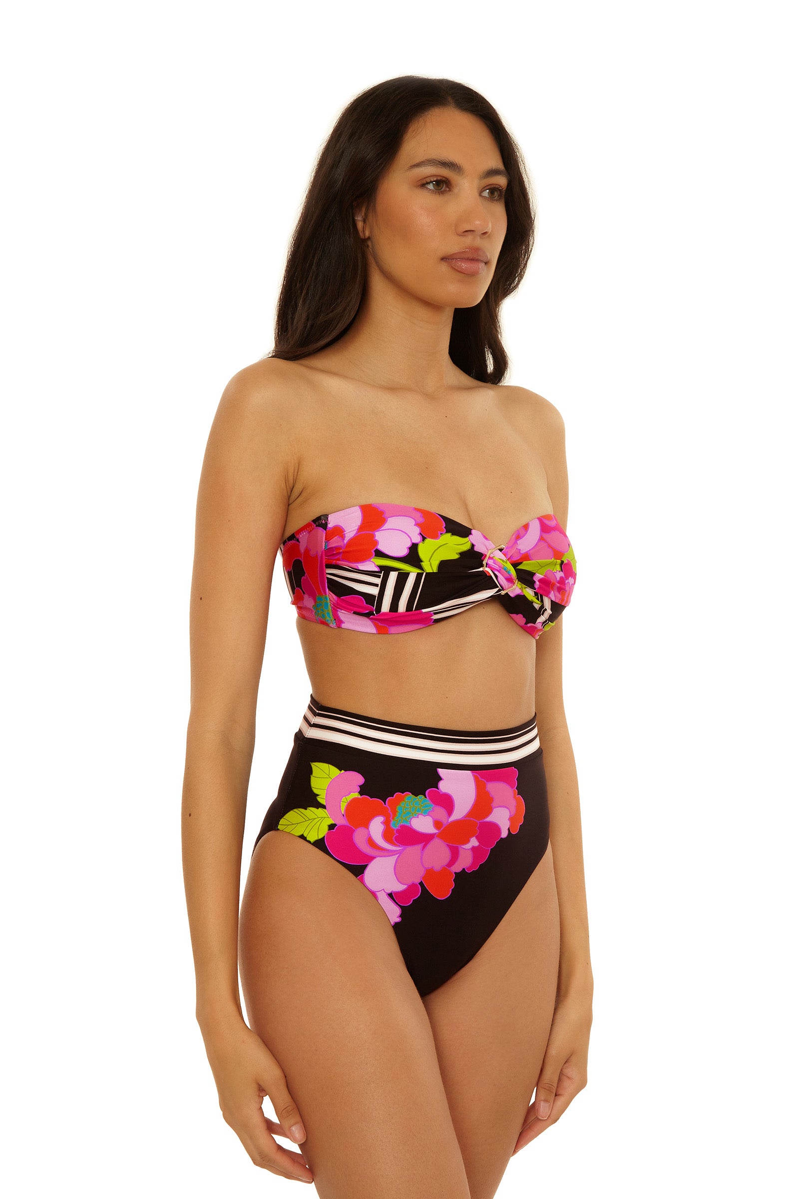 A woman models the Twist Bandeau Swim Top - Bougainvillea, featuring a strapless, colorful floral design with pink, green, and yellow hues and high-waisted bottoms, standing against a white background.
