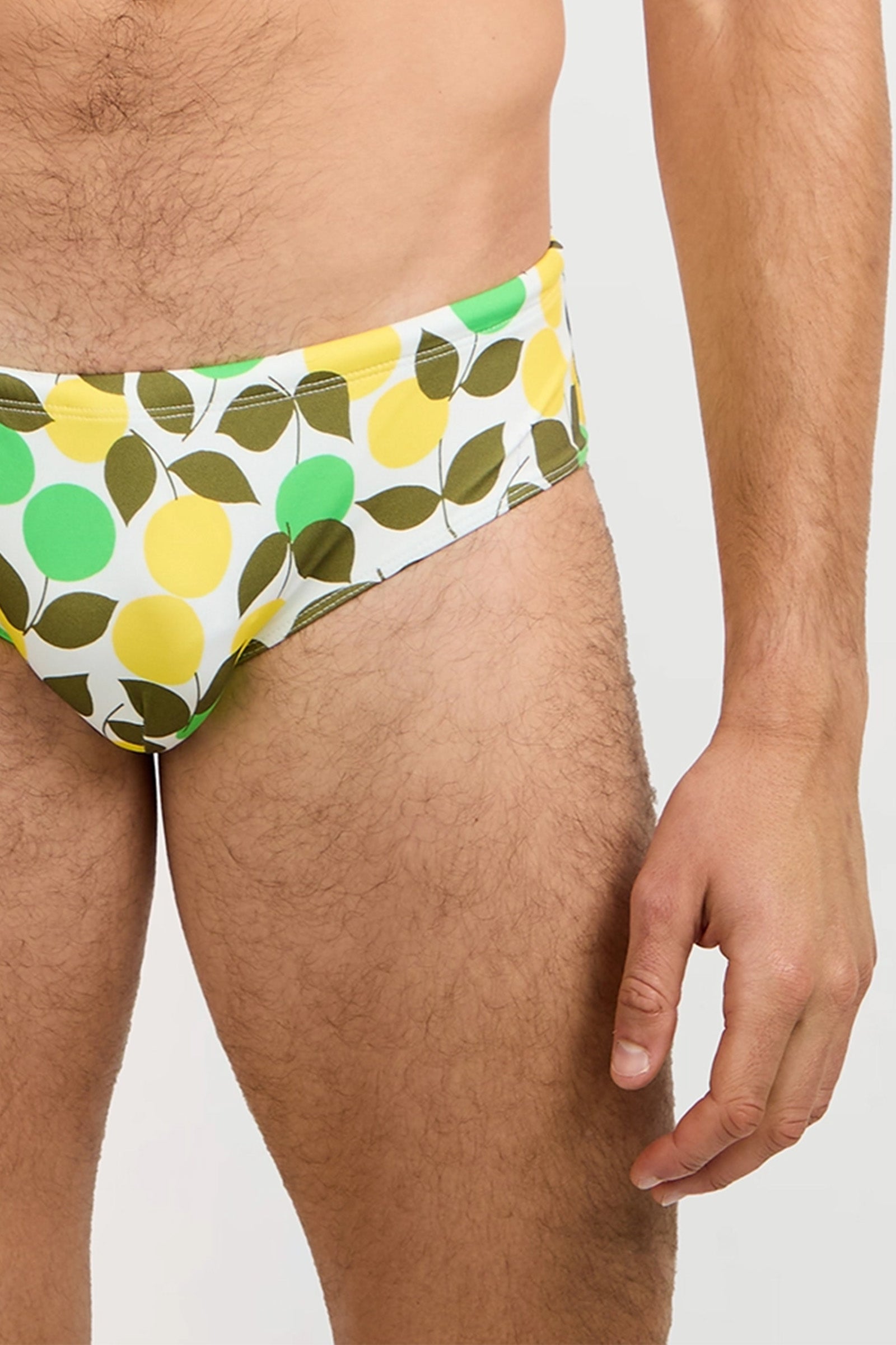 A person models the Bondi Swim Brief - Limone, featuring green and yellow circles with olive-green leaves; the photo captures their lower torso, upper thighs, and one arm at their side.