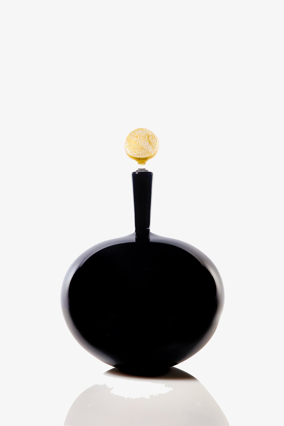 A glossy, black Carmella Barware Low Round with a round, textured gold cap sits on a reflective surface against a plain white background.