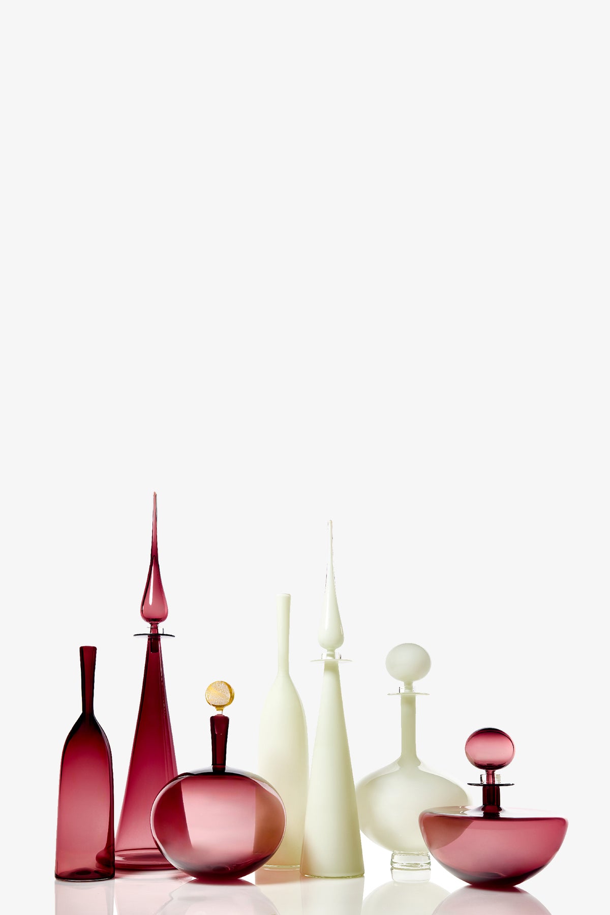 A row of Carmella Barware Low Round glasses in deep pink and white, featuring elegant shapes and sculptural stoppers, displayed against a white background.