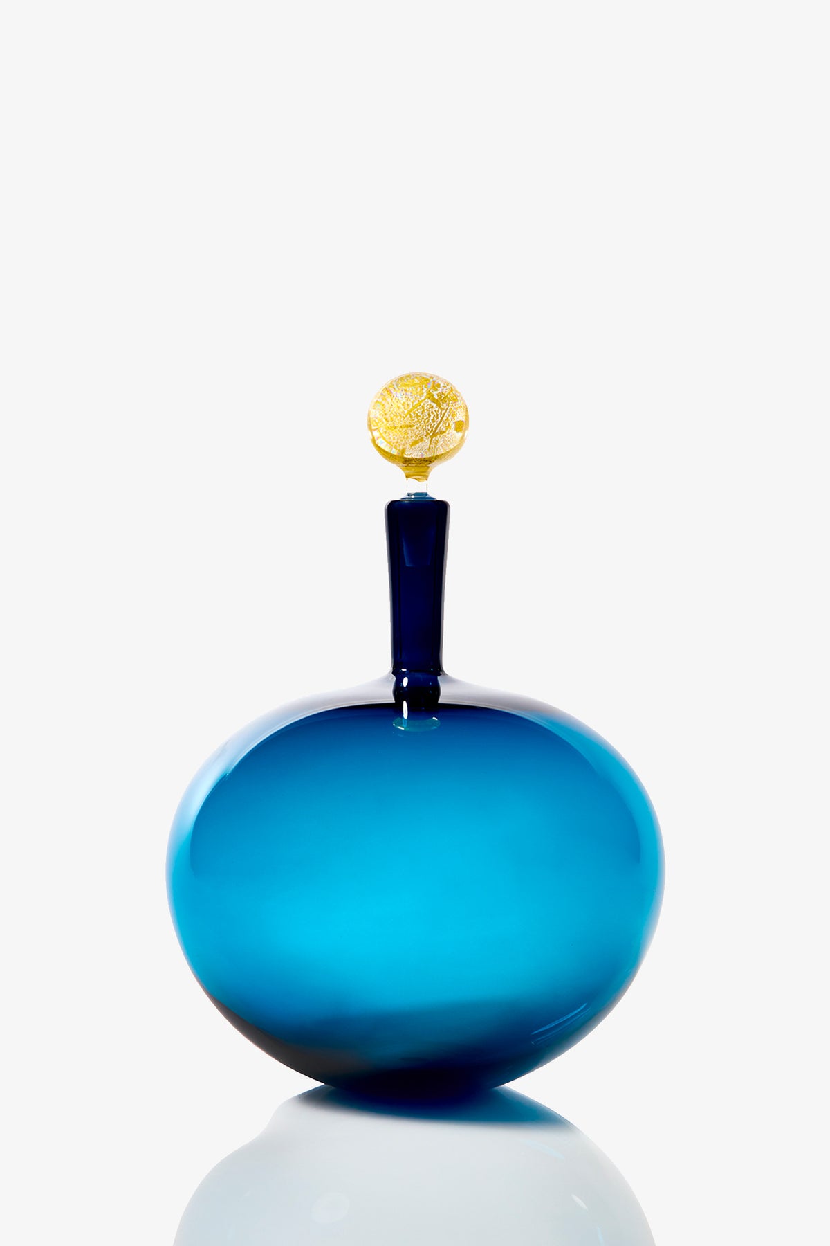 The Carmella Barware Low Round is a blue glass bottle with a rounded shape, narrow neck, and gold decorative stopper shaped like a textured disc, displayed against a plain white background.