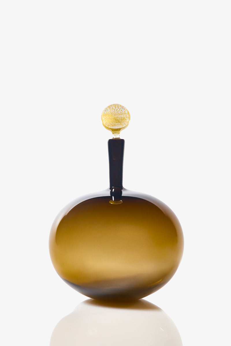 The Carmella Barware Low Round is an amber glass bottle with a narrow neck, golden decorative stopper, and glossy finish, displayed against a white background.