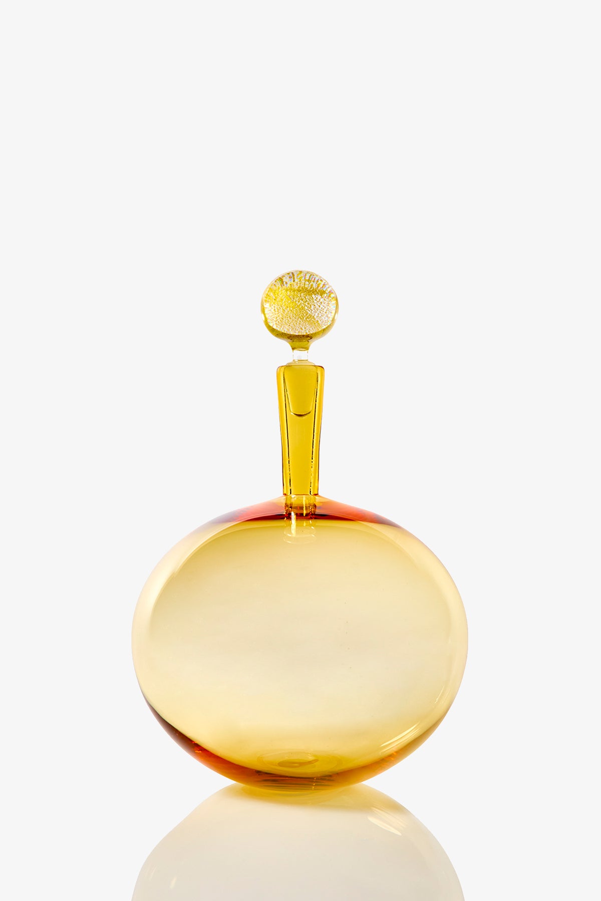 The Carmella Barware Low Round is a round, golden-yellow glass bottle with a flat base and a tall, narrow stopper topped with a textured circular design, displayed against a plain white background.