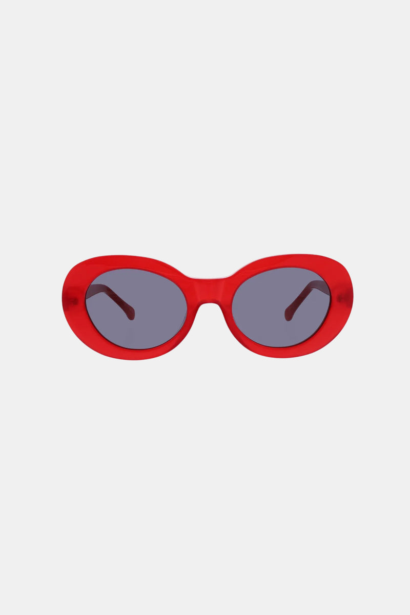 The Carova Sunglass features bold, oval-shaped red frames with dark tinted lenses, showcased against a plain white background.