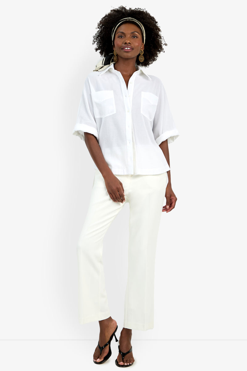 A woman stands confidently against a plain white background wearing the Hawaii Top, white pants, black sandals, gold earrings, and a patterned headband.