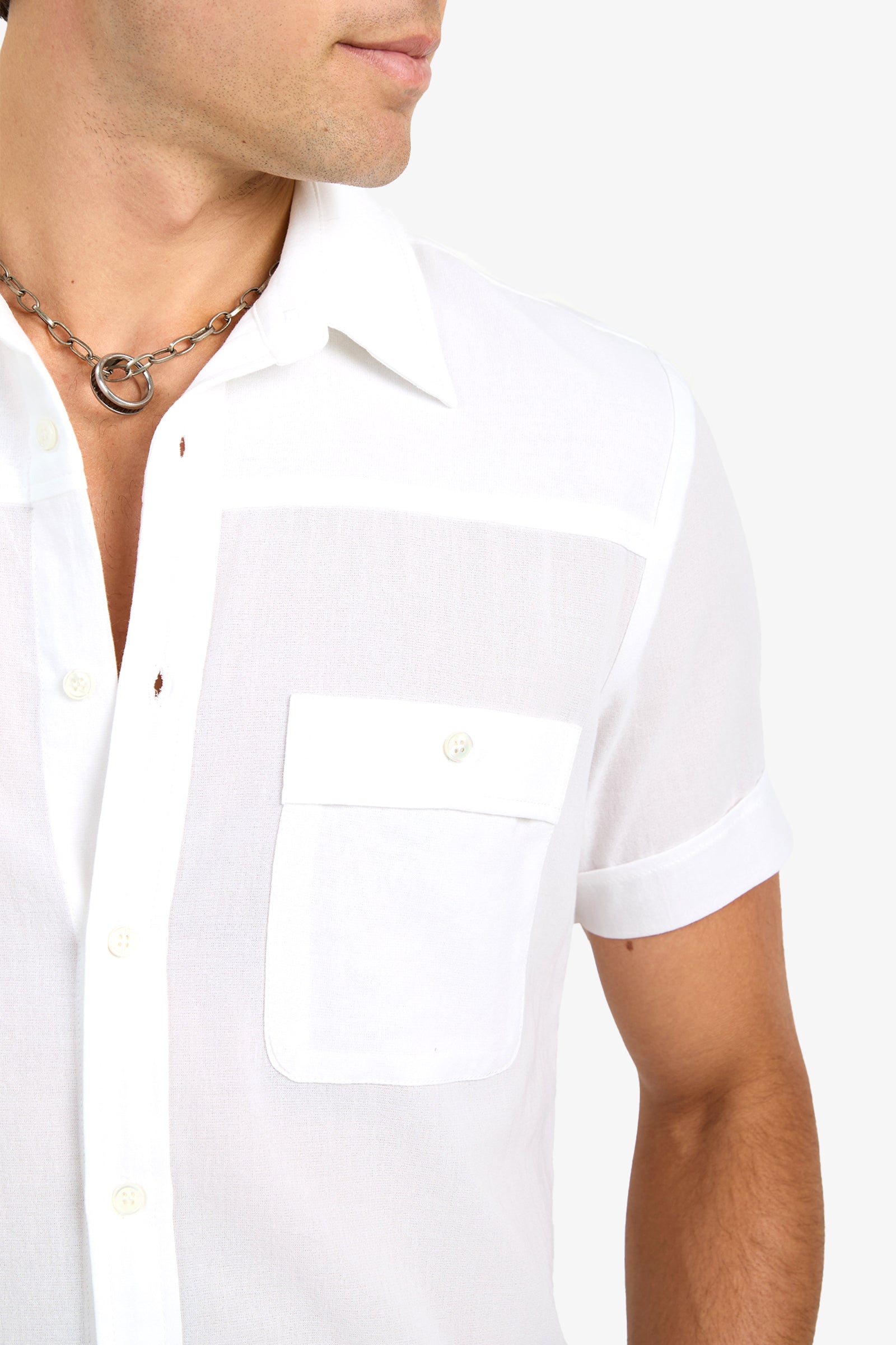 A man wearing the Will Shirt, a short-sleeve white button-up with a chest pocket, and a silver chain necklace, shown from the shoulders up against a plain white background.