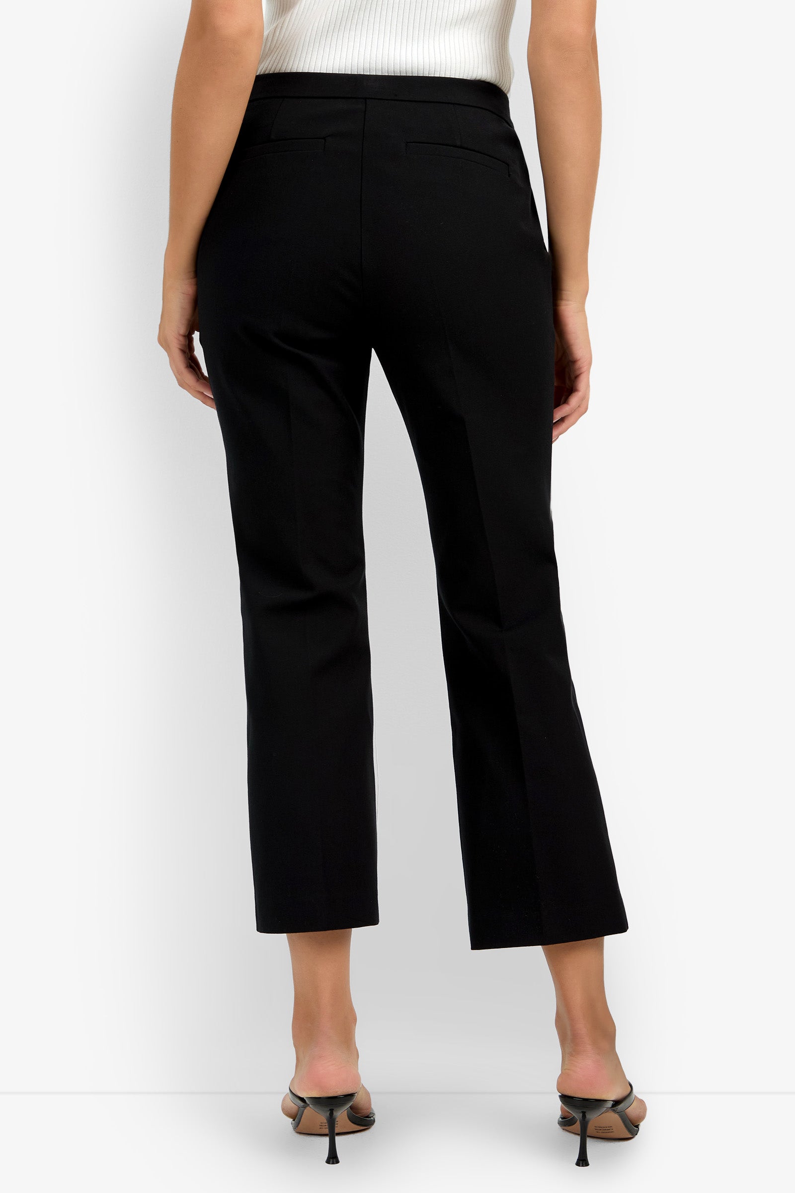 A woman shown from the back wears the Lulu Pant in black, paired with black heeled sandals and a white sleeveless top.