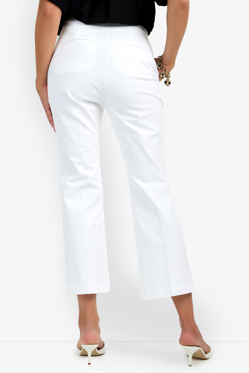 A person is seen from the back wearing Lulu Pant in white and white heeled sandals, with one hand on their hip and the other holding sunglasses, against a plain white background.