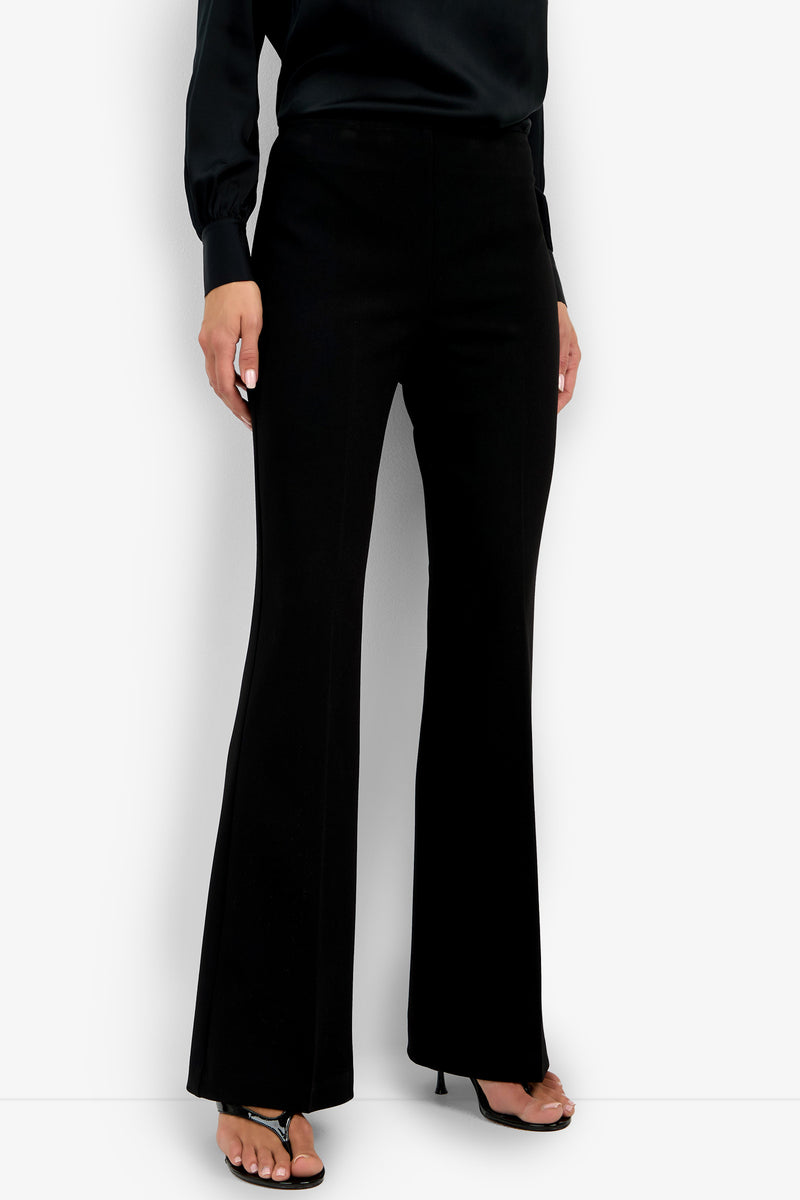A person showcases the Chimayo Pant—black flared dress pants—paired with a black blouse and black high-heeled sandals, standing against a plain white background. The focus is on the lower half of the outfit.