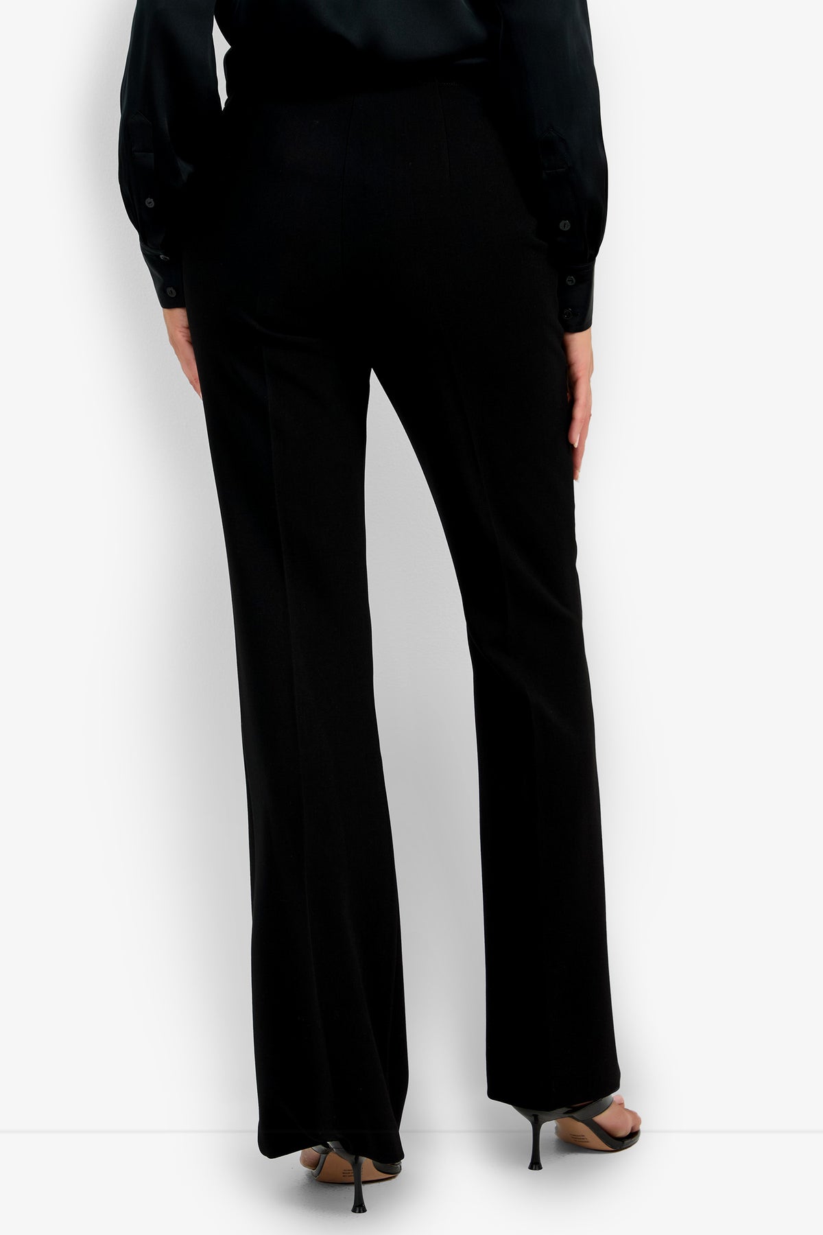 A person is shown from the back wearing the tailored, slightly flared Chimayo Pant in black with black heeled sandals and a black long-sleeve shirt.
