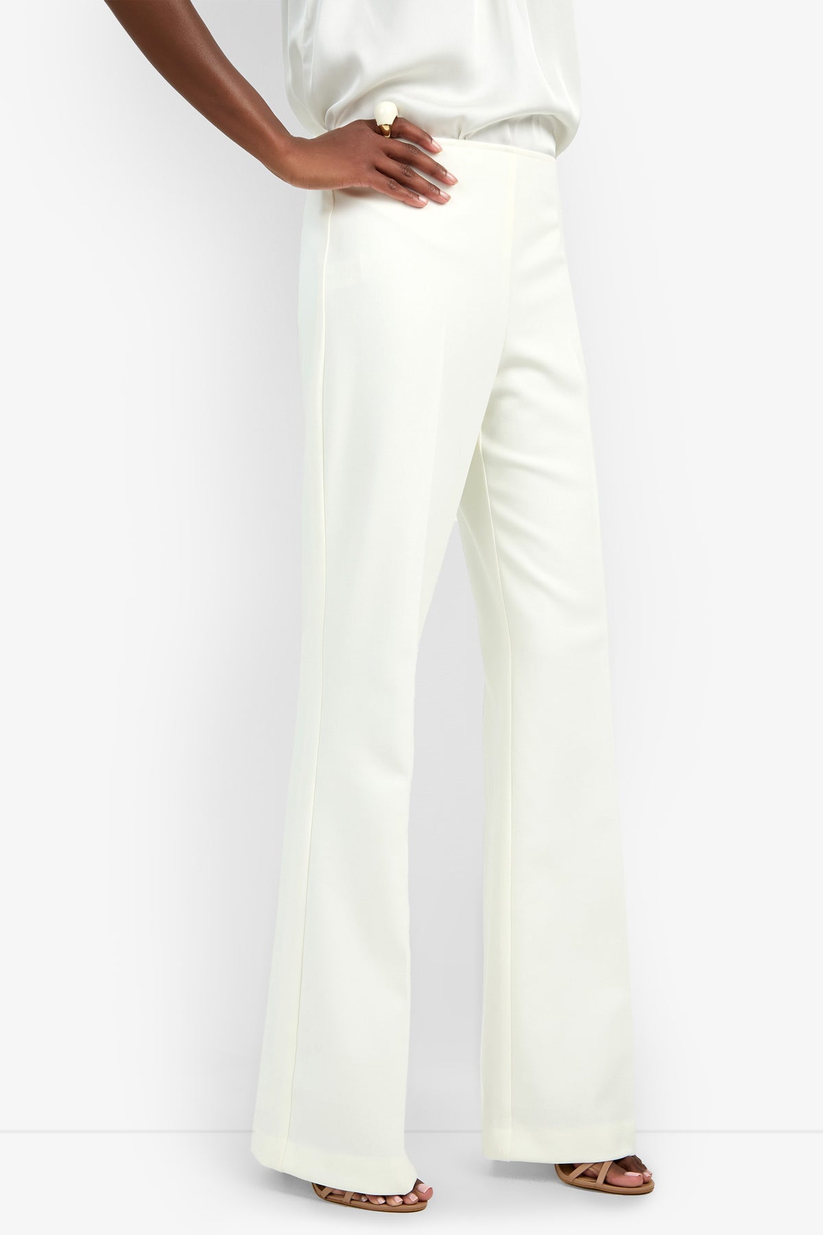 Wearing the Chimayo Pant—high-waisted, wide-leg, and white—with open-toe heels and a matching white top, a person poses confidently with one hand on their hip against a plain white background.