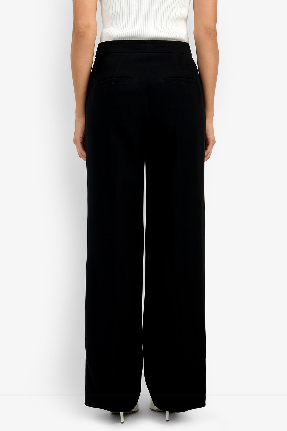 Someone is shown from the back against a plain white background, wearing the Sadie Pant—high-waisted, wide-leg black trousers—and a white ribbed sleeveless top.