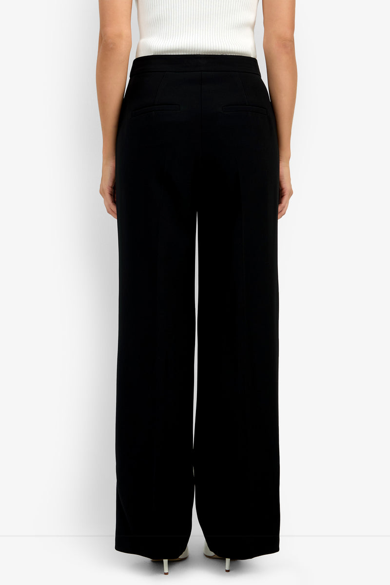 Someone is shown from the back against a plain white background, wearing the Sadie Pant—high-waisted, wide-leg black trousers—and a white ribbed sleeveless top.