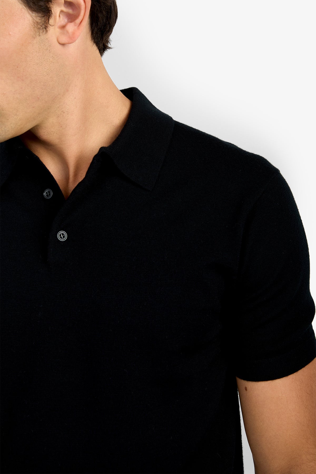 A man models the Grant Short Sleeve Polo—black, with a collar and buttons—shown from shoulders to mid-torso against a plain white background. His face is partially out of frame.