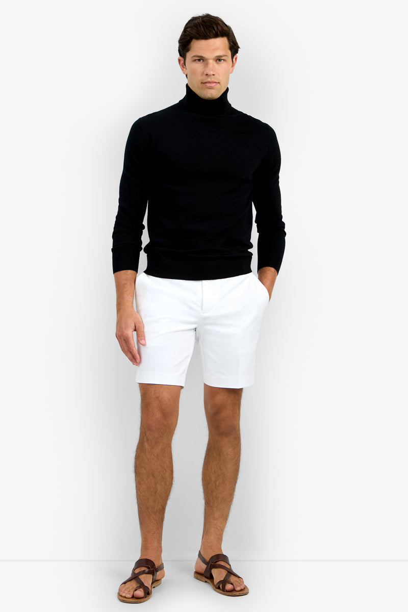 A man stands against a plain background wearing the Roy Long Sleeve Turtleneck, white shorts, and brown sandals.