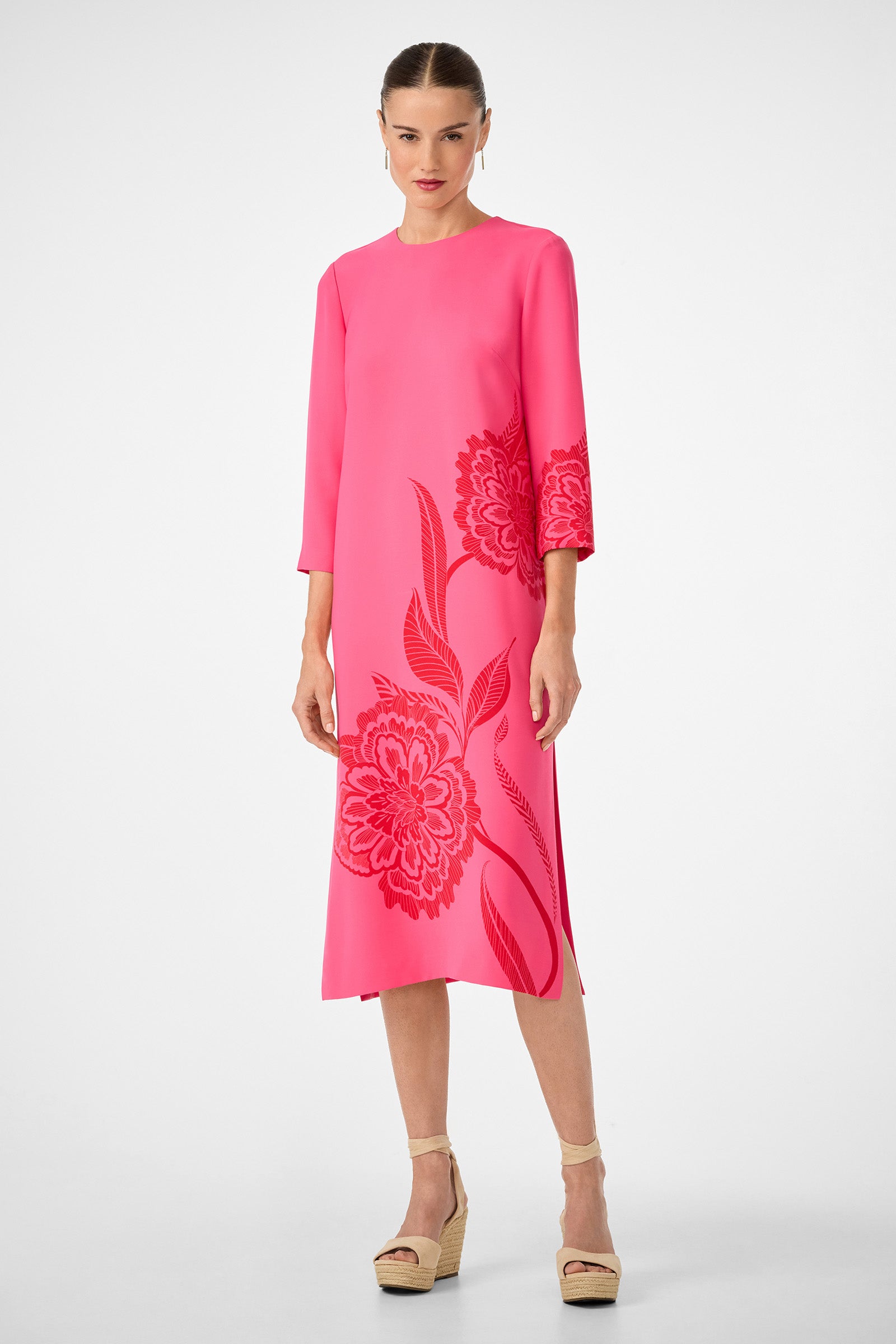 A woman models the Cointreau 2 Dress—a bright pink, knee-length dress with three-quarter sleeves and bold floral patterns—paired with beige wedge sandals against a white background.