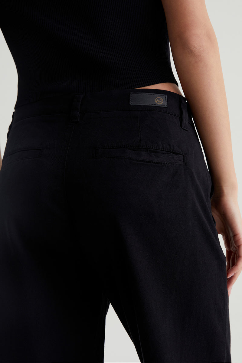 A person wearing the AG Caden Wide Leg Pant in black, shown from the waist down and behind, with one arm relaxed at their side.