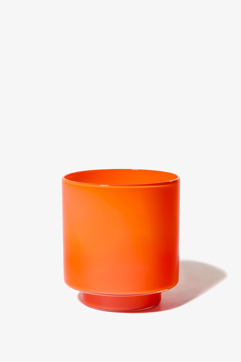 The Fiorelli Low Container, a bright orange cylindrical planter with a smooth surface, sits on a white background and casts a soft shadow to the right.