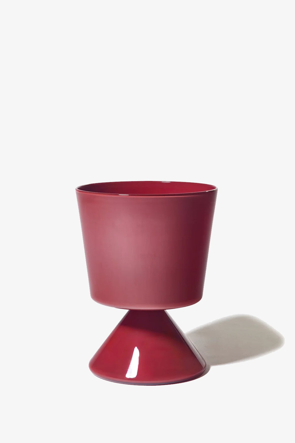 The Fiorelli Low Taper is a modern, glossy red planter featuring a wide, cylindrical top and a cone-shaped base, shown casting a shadow to the right against a plain white background.