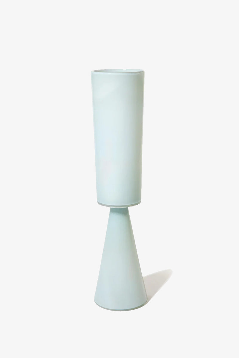 The Fiorelli Tall Cylinder is a modern, light blue ceramic vase featuring a tall cylindrical top and a conical base, shown standing upright against a plain white background.