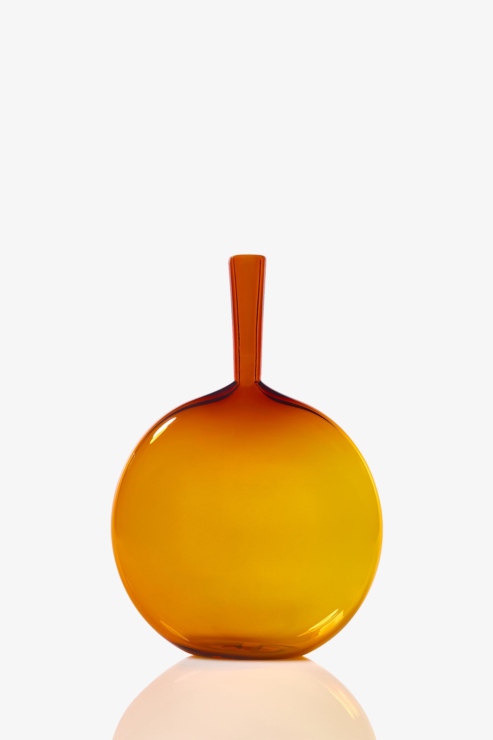 The Flask Angelic Bottle is a round, flat, amber-colored glass vase with a narrow neck, shown standing upright on a white background and softly reflecting on the surface beneath it.